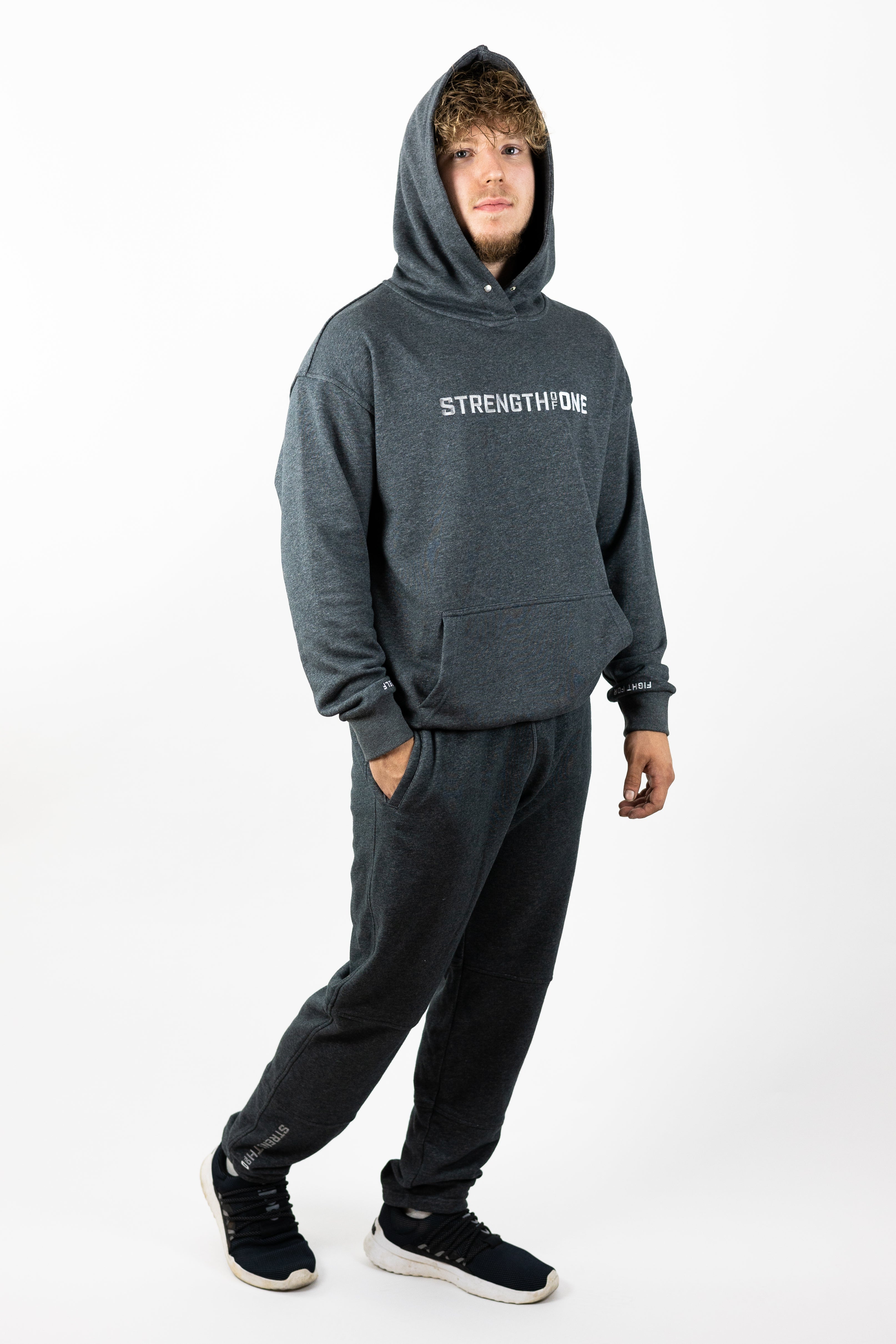 Man walking with hand in pocket wearing gray hoodie with hood up and gray sweatpants