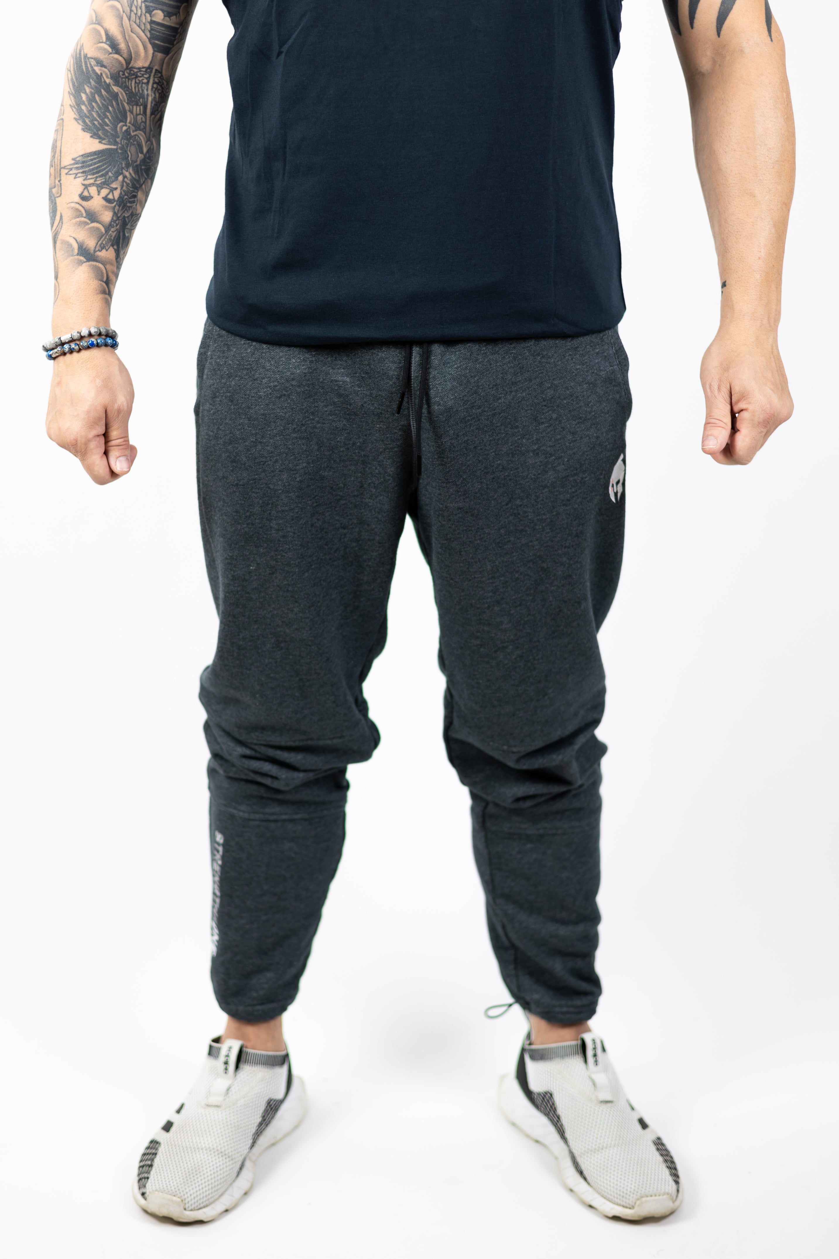 man modeling Strength of One gray sweatpants with embroidered helmet logo at top right hip and Strength of One logo vertical down left lower leg