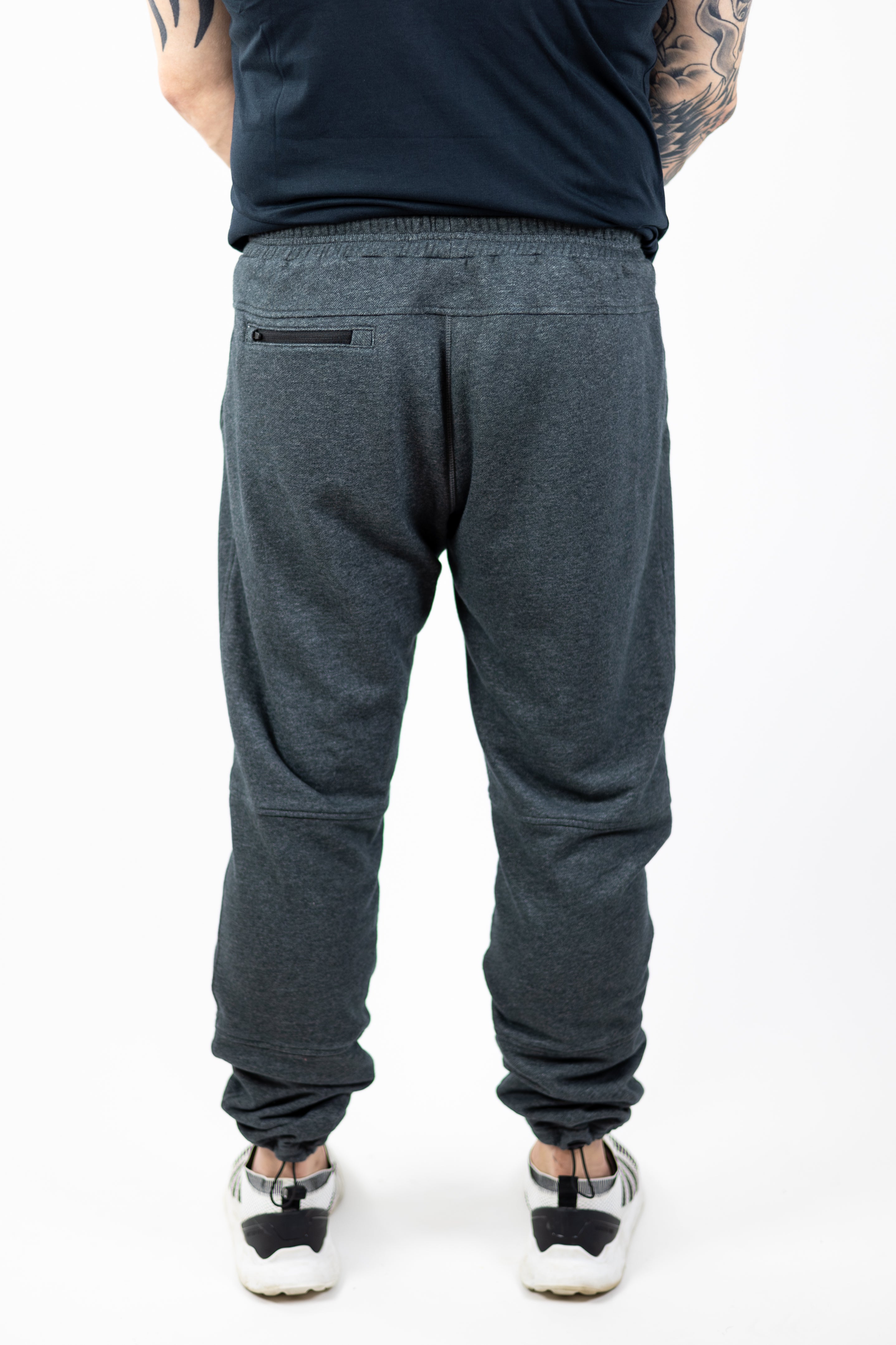 rear view of man modeling Strength of One gray sweatpants with embroidered helmet logo at top right hip and Strength of One logo vertical down left lower leg