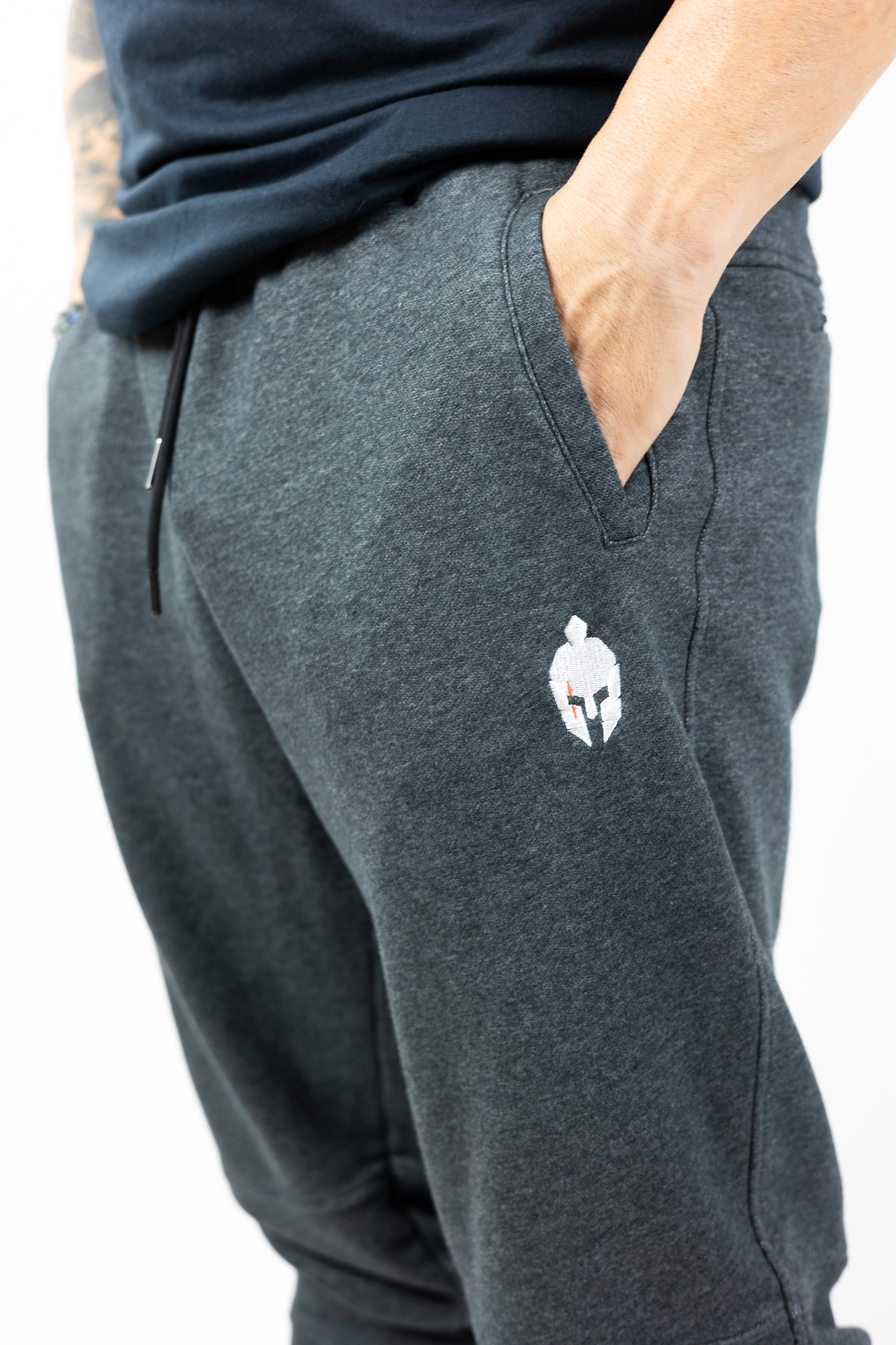 man modeling gray sweatpants with embroidered helmet logo at top right hip and Strength of One logo vertical down left lower leg