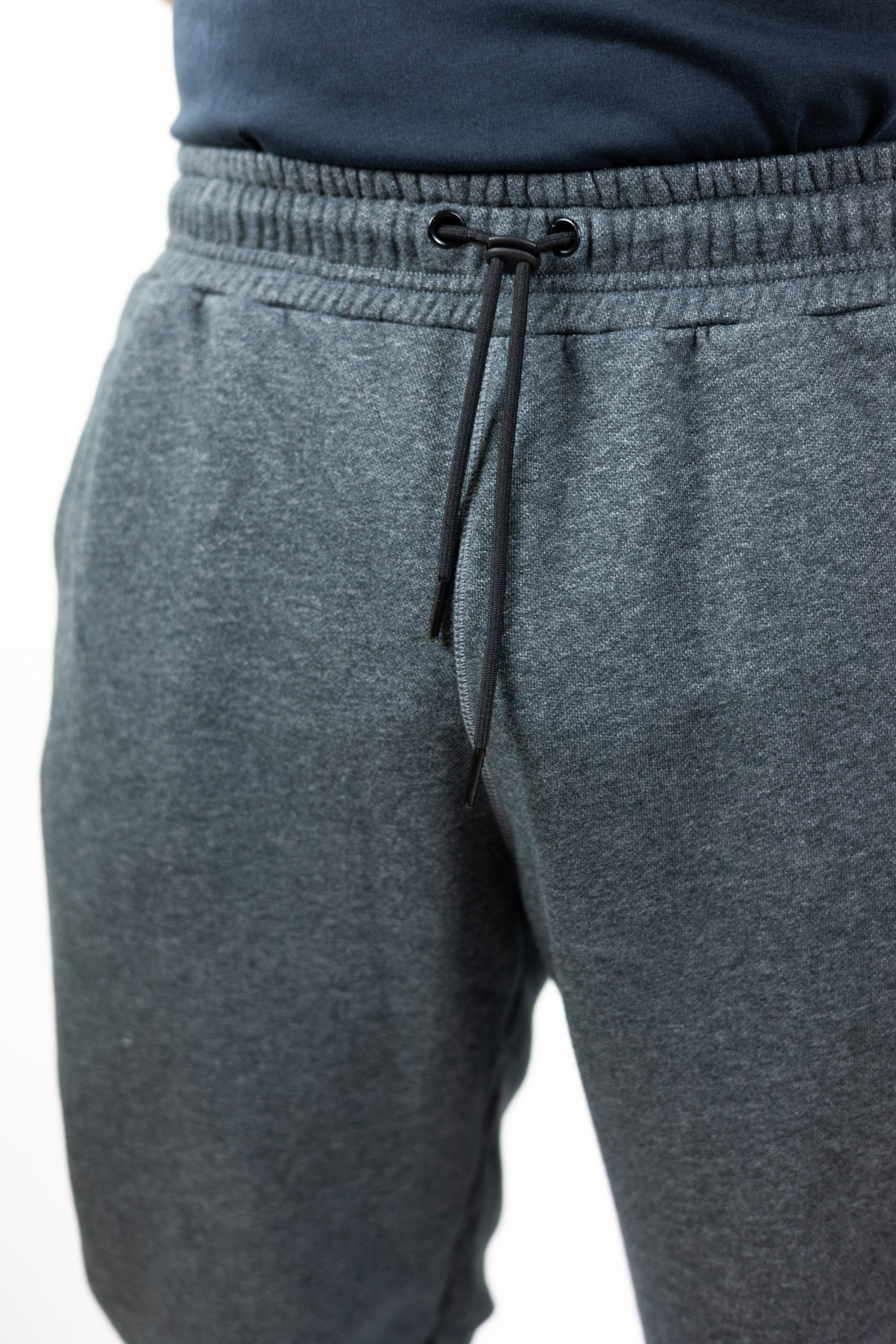 man modeling gray sweatpants with embroidered helmet logo at top right hip and Strength of One logo vertical down left lower leg