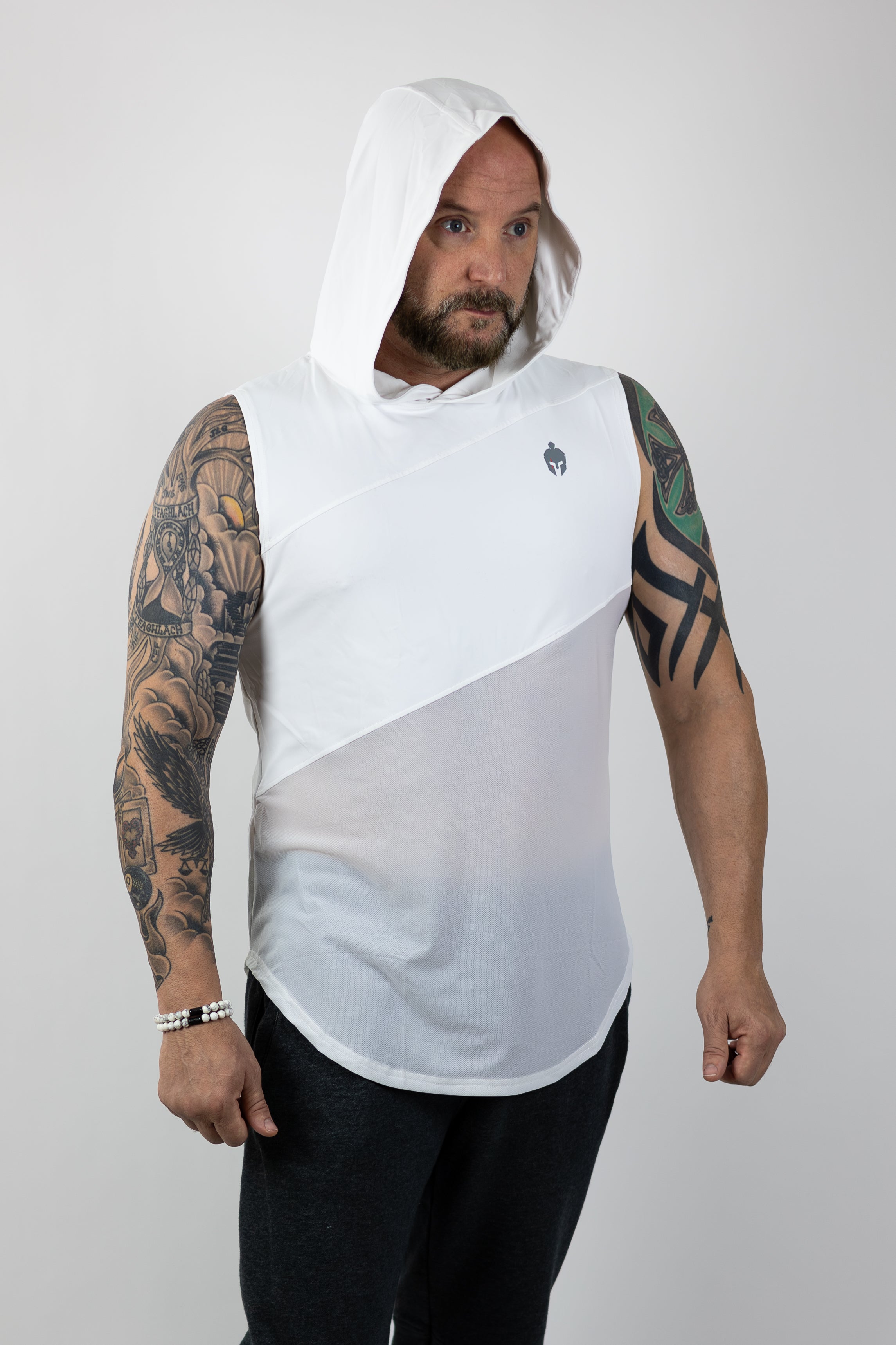 A man with tattoos on his arms stands confidently in a white Strength of One shirt with hood over head and gray sweatpants