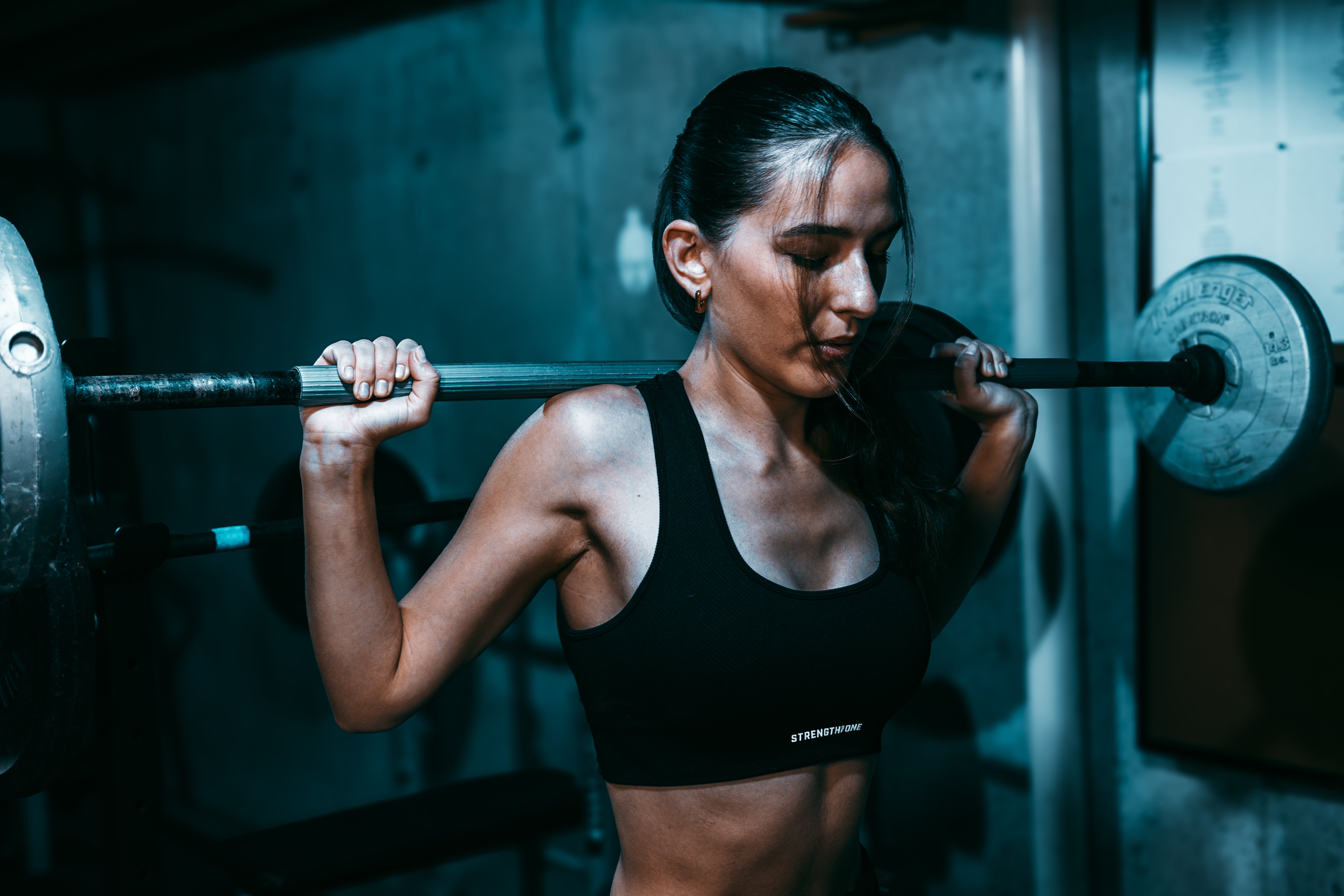 Woman wearing black Strength of One sports bra performing squats with barbell