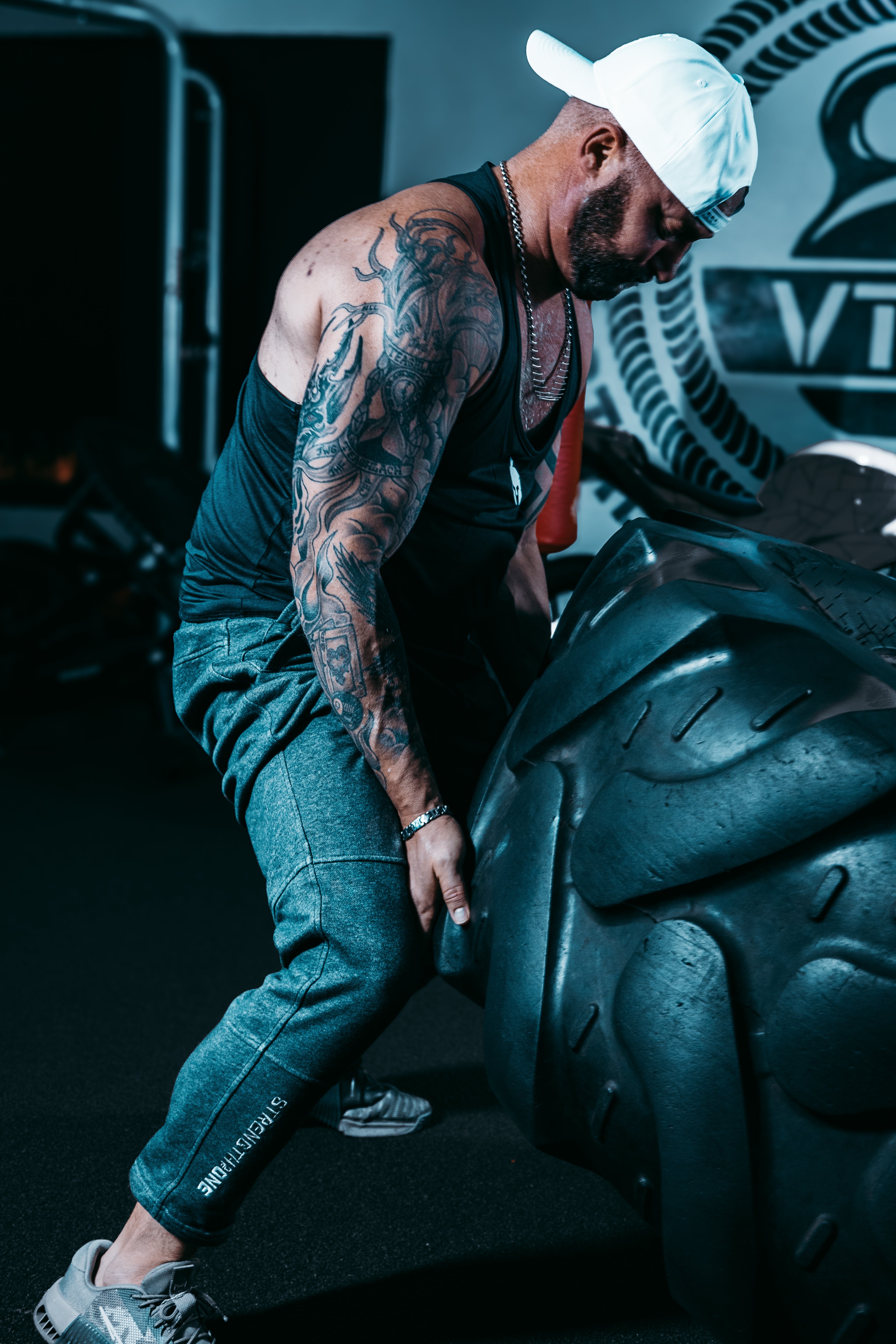 Man in Strength of One workout clothes performing a tire flip in gym