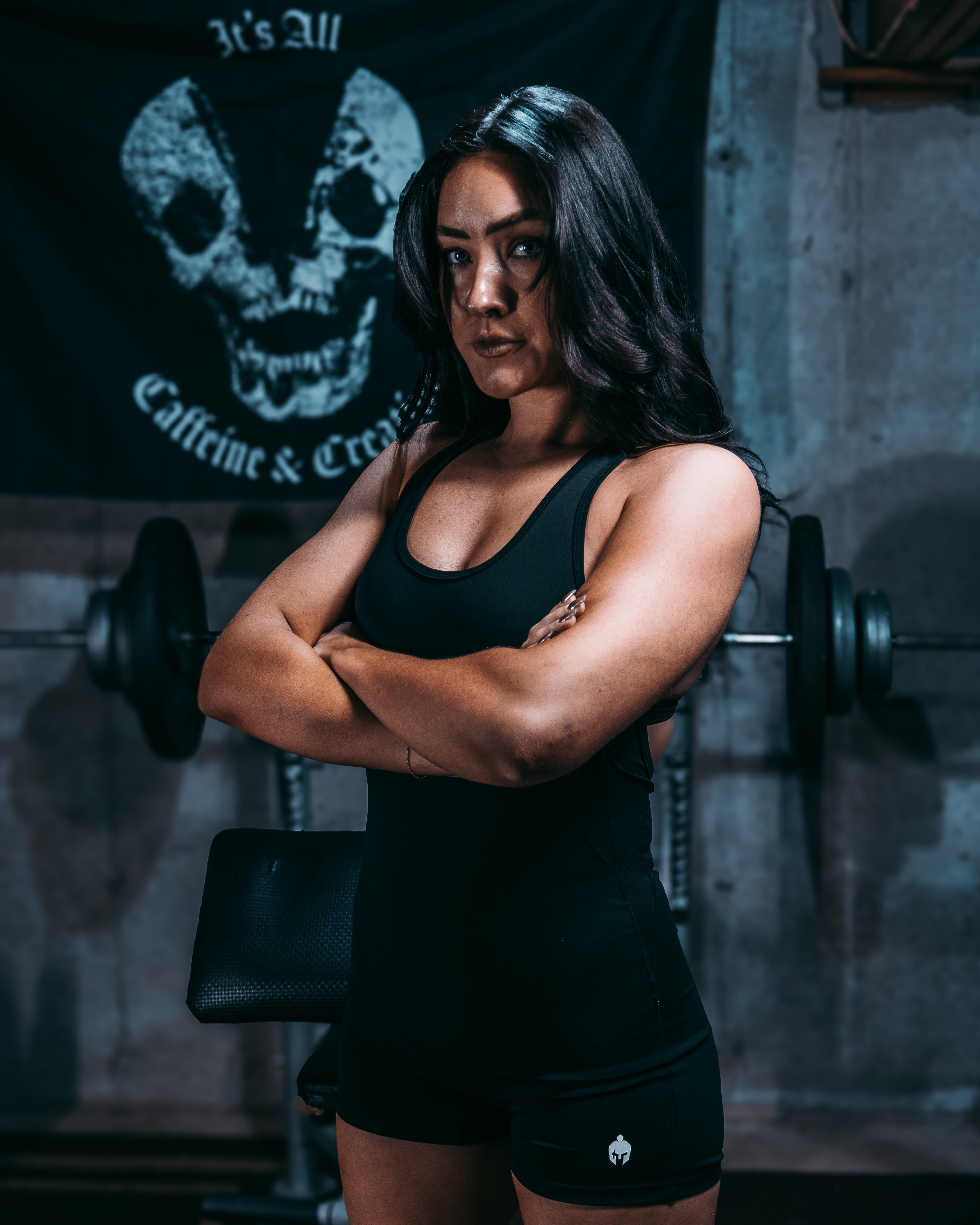 Woman standing in gym with arms crossed wearing Strength of One workout romper