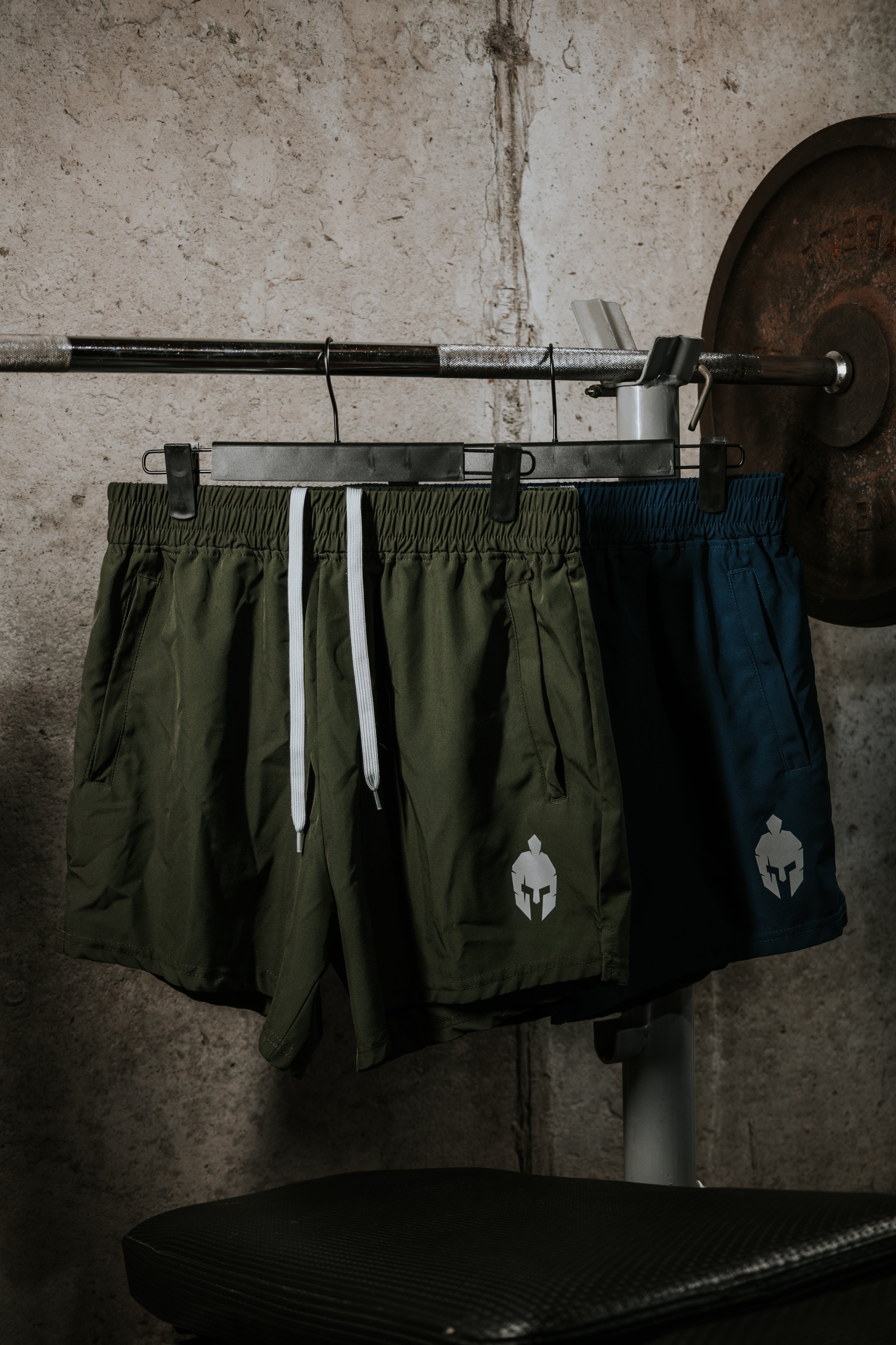 Green and navy Strength of One workout shorts with Spartan logo hanging on gym weight rack