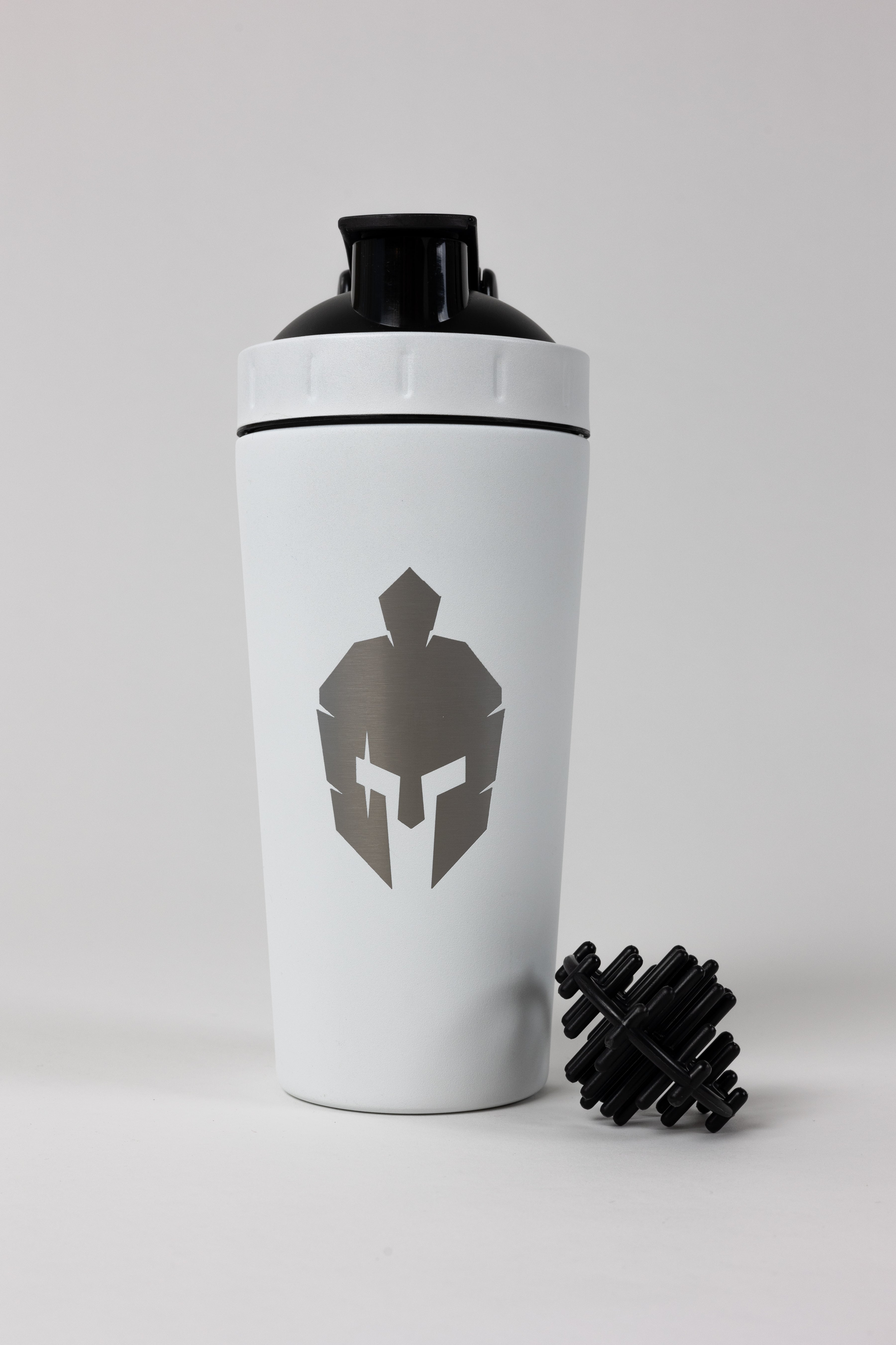White metal shaker bottle with roman helmet logo on front and black shaker ball sitting next to bottle