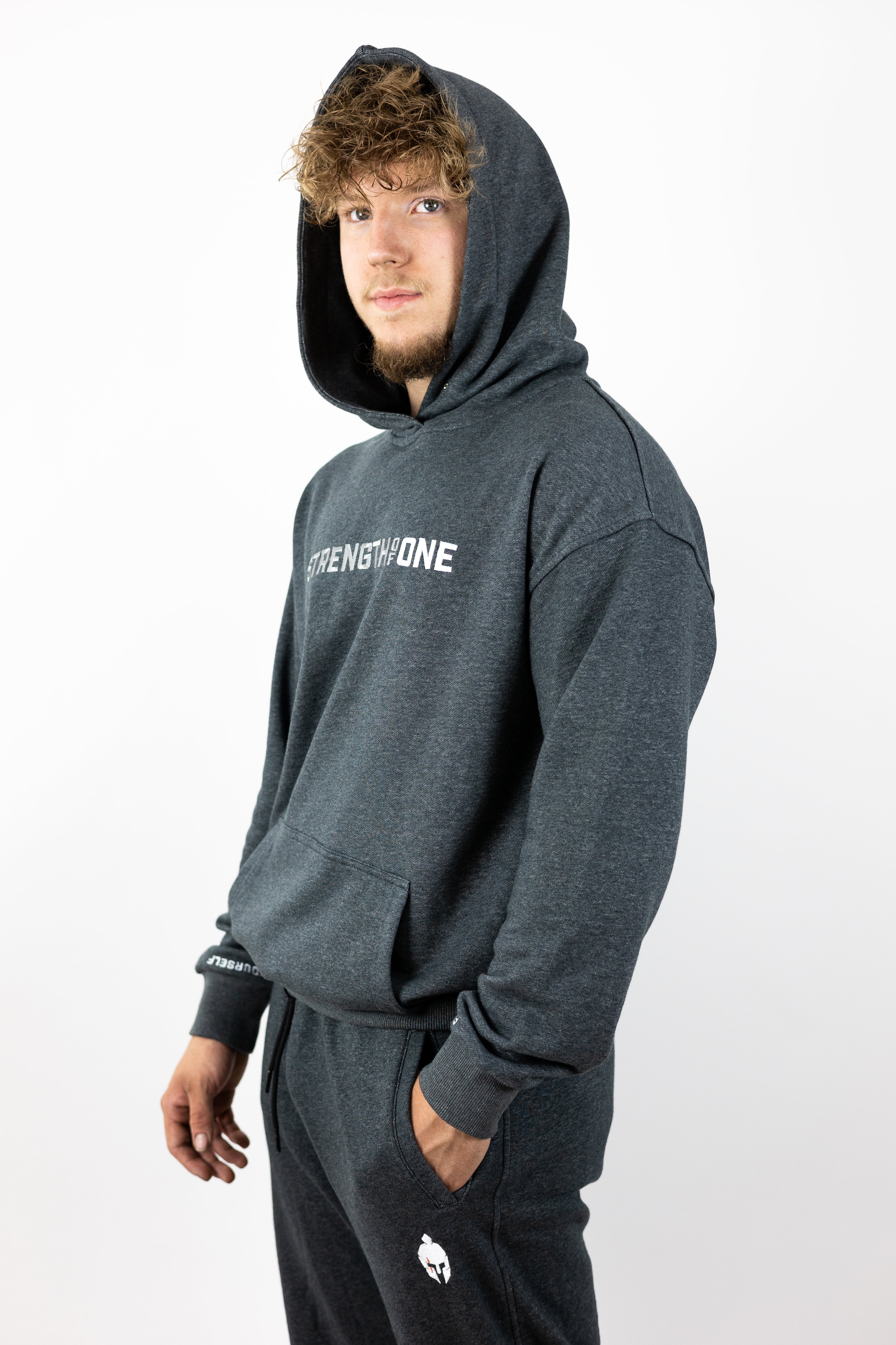 Man looking into distance slightly turned and wearing gray hoodie with words Strength of One across chest