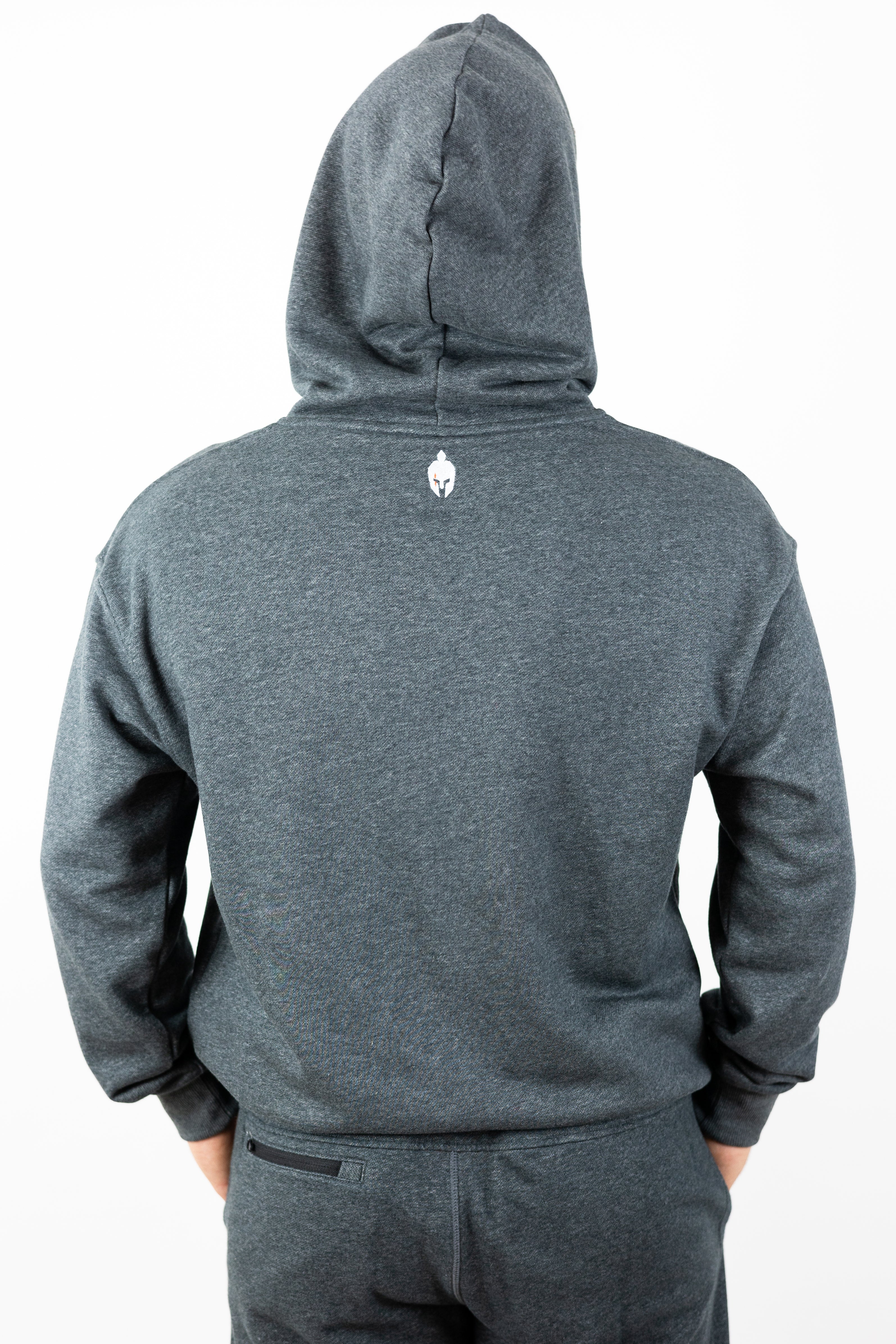 Man wearing gray hoodie with hood up and small helmet logo embroidered below hood neckline