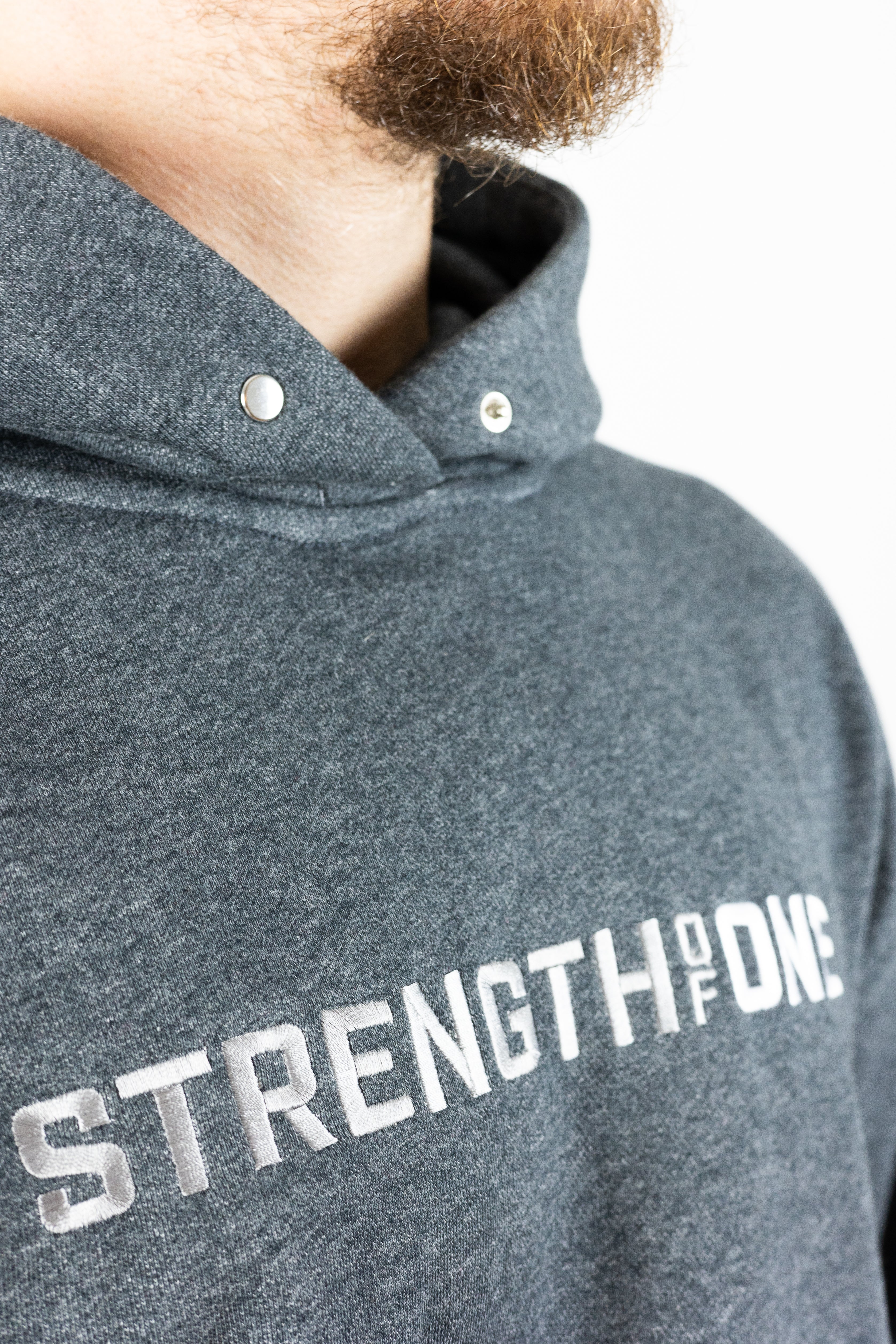 Gray hoodie with metal clasp at neck and words Strength of One embroidered on center chest