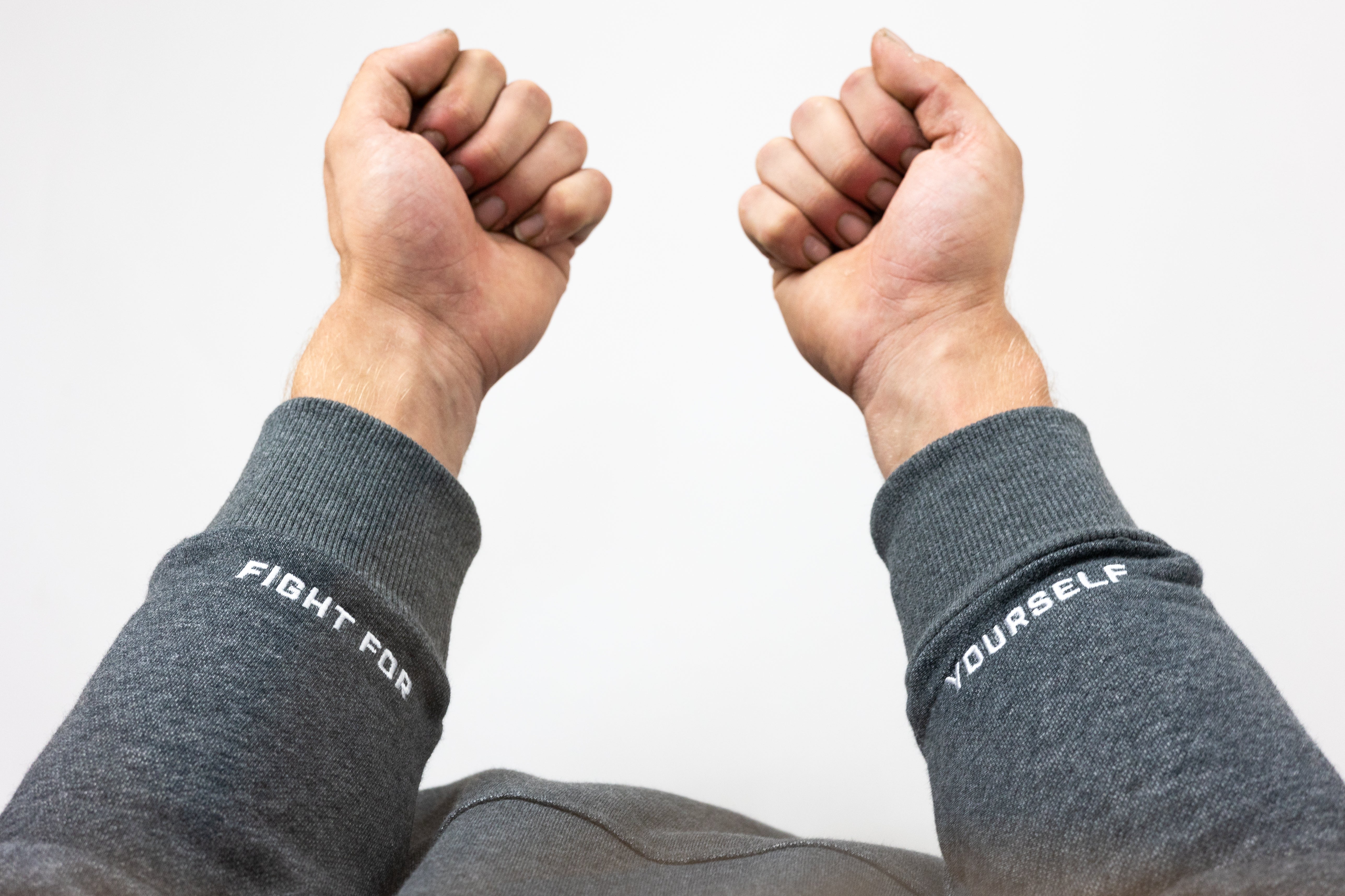 Two arms with hands clenched in fists wearing gray hoodie with text "Fight For" and "Yourself" on fabric at wrist