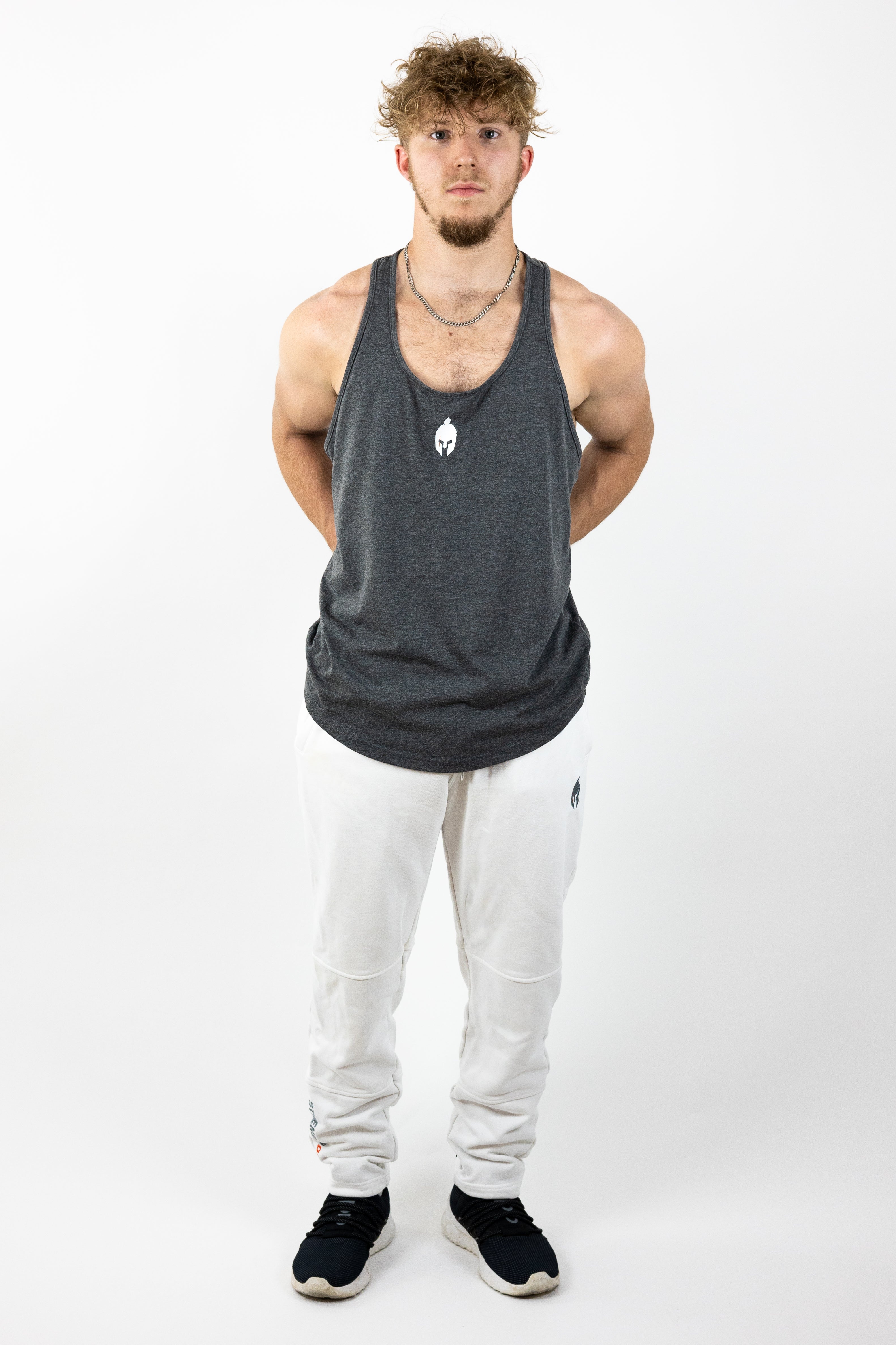 Man wearing gray stringer and white sweatpants posed with hands behind back