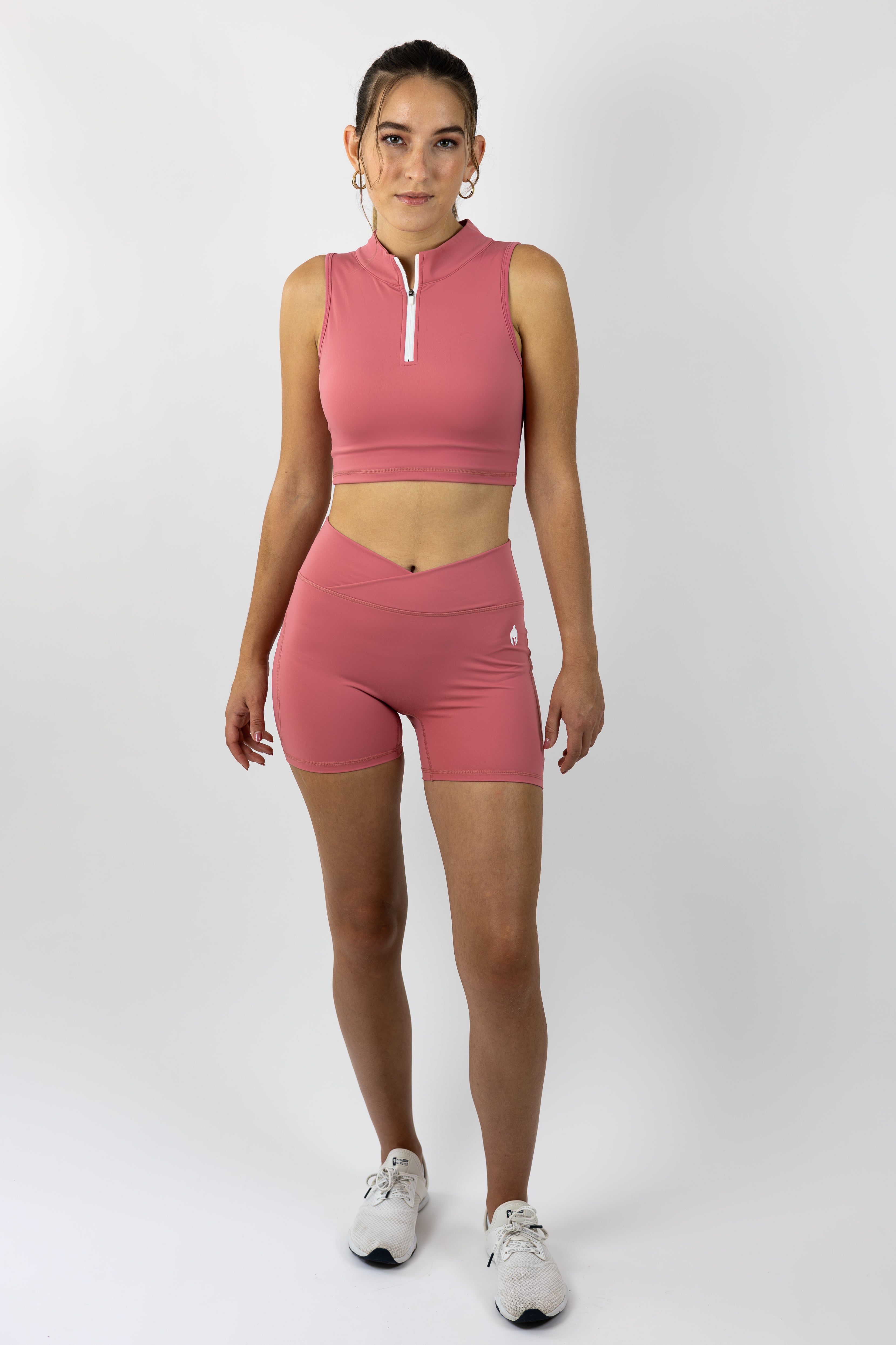 woman modeling medium pink 3/4 zip Strength of One gym top and matching medium pink form fitting gym shorts with warrior logo on right hip
