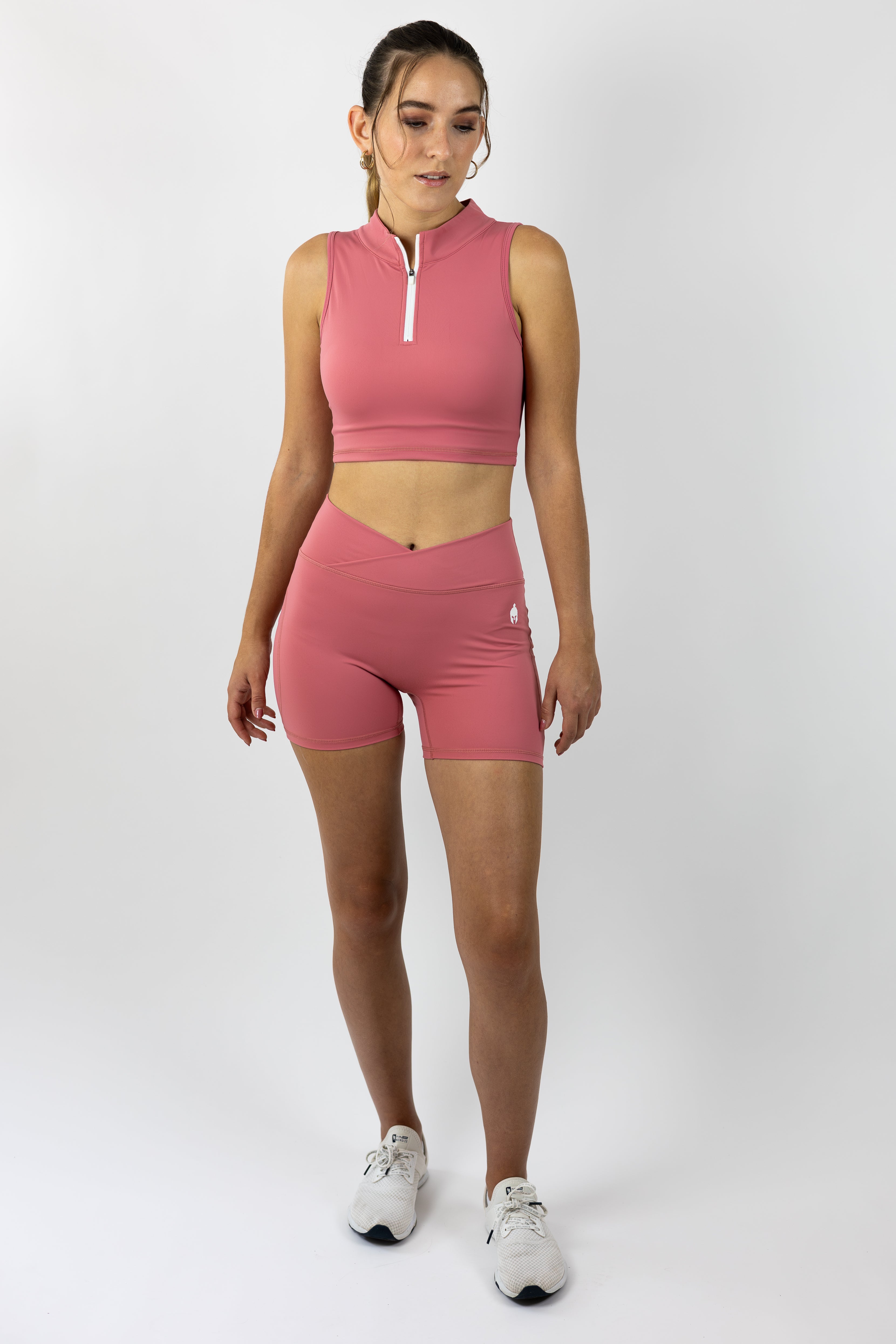 Woman modeling medium pink collared Strength of One gym wear top with white 3/4 zipper and medium pink tight gym wear shorts with cross over top band