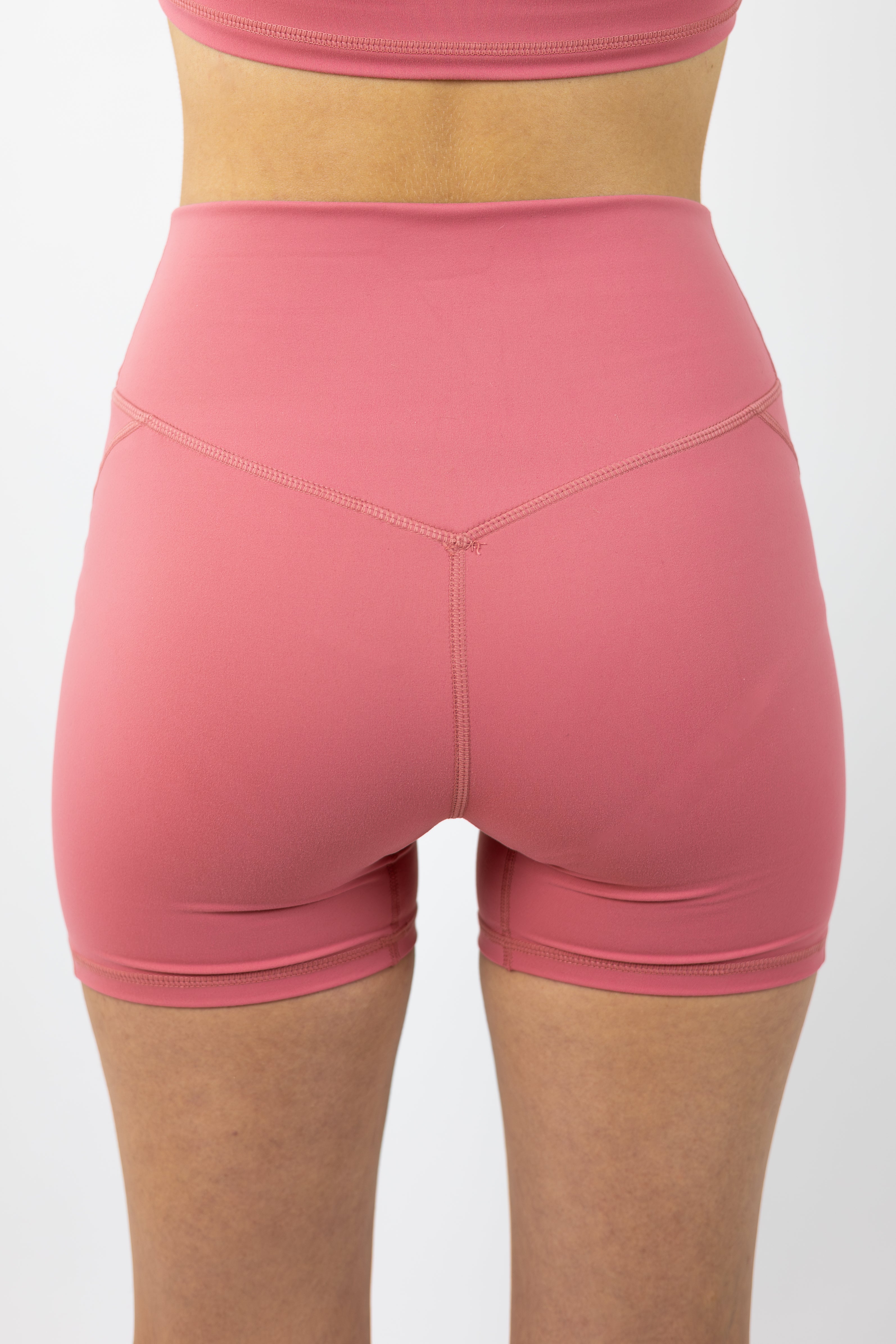 rear view of medium pink form fitting Strength of One gym shorts modeled by woman