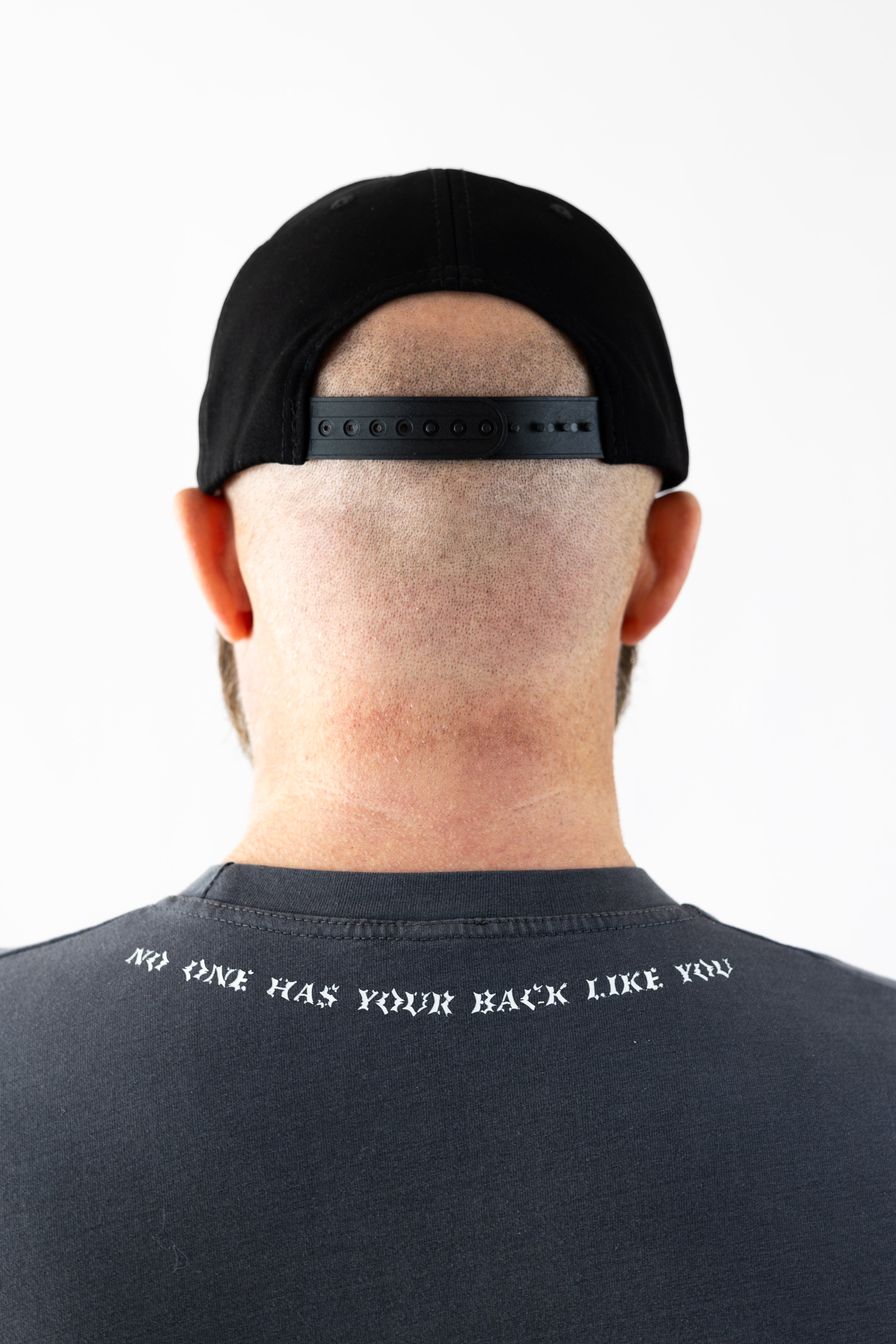 Rear view of a person wearing a black Strength of One cap and a t-shirt with text "no one has your back like you".