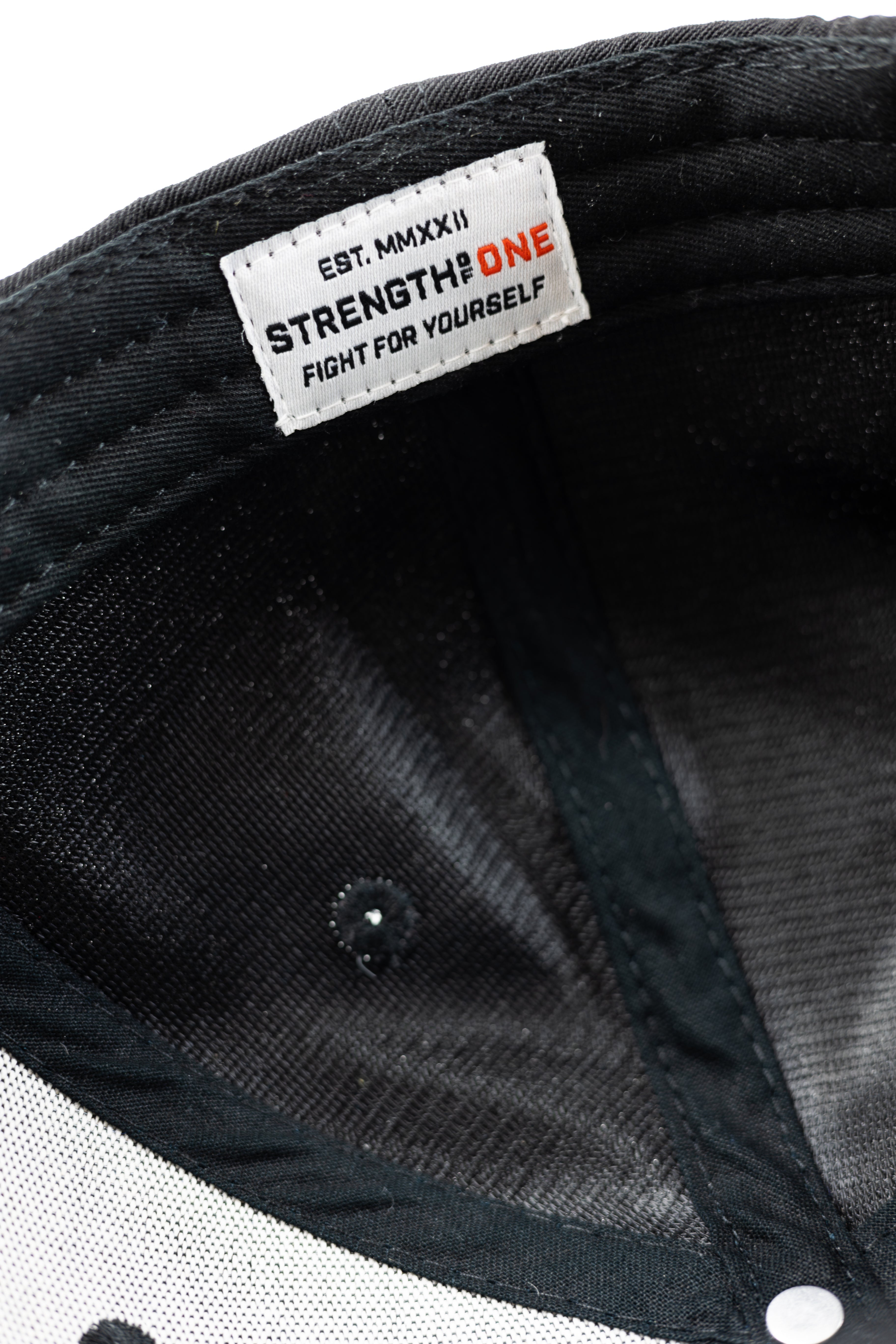 Close-up of a black Strength of One cap with a "strength of one" brand label on the inside.