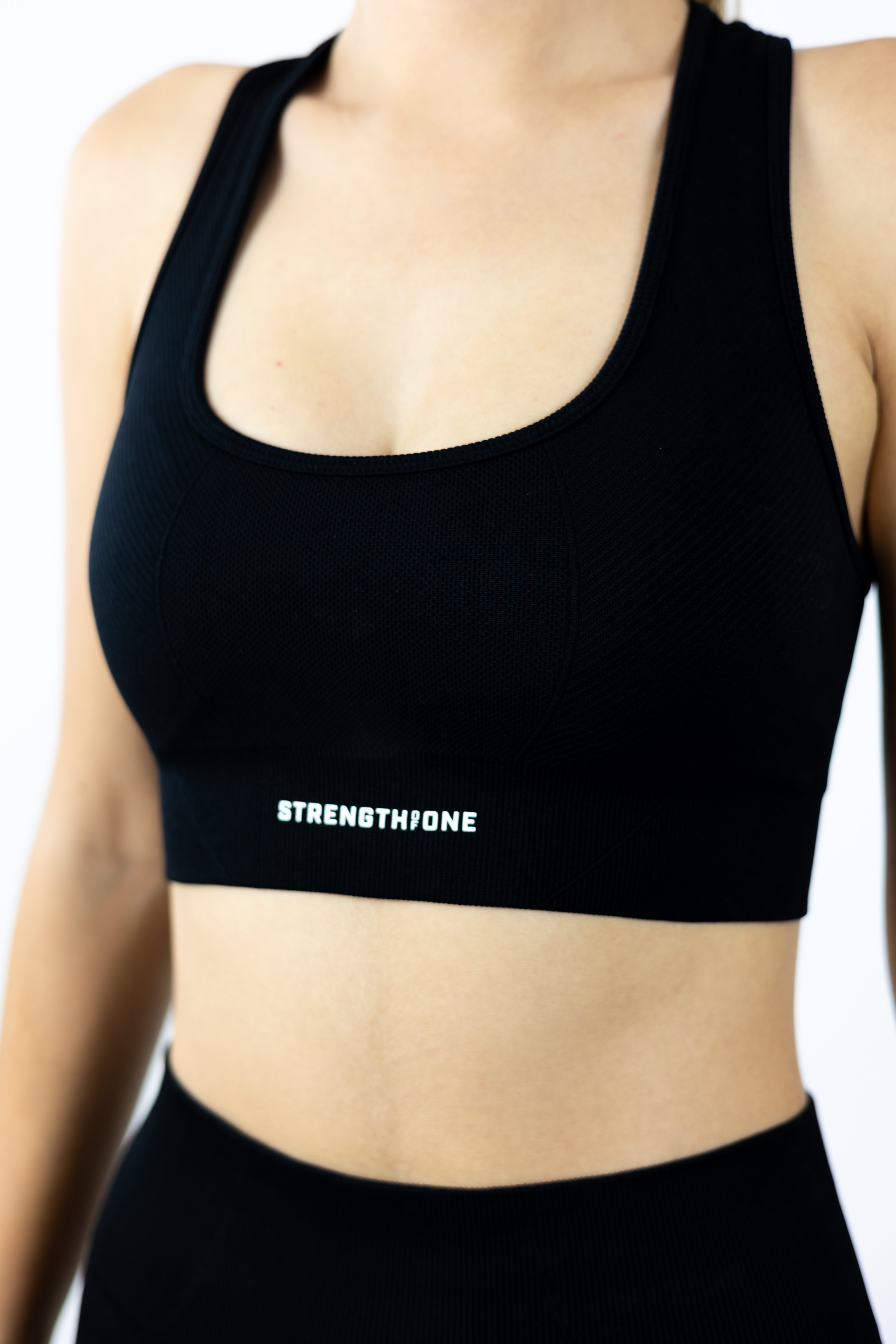 woman modeling Strength of One black sports bra with 3D raised logo on lower band