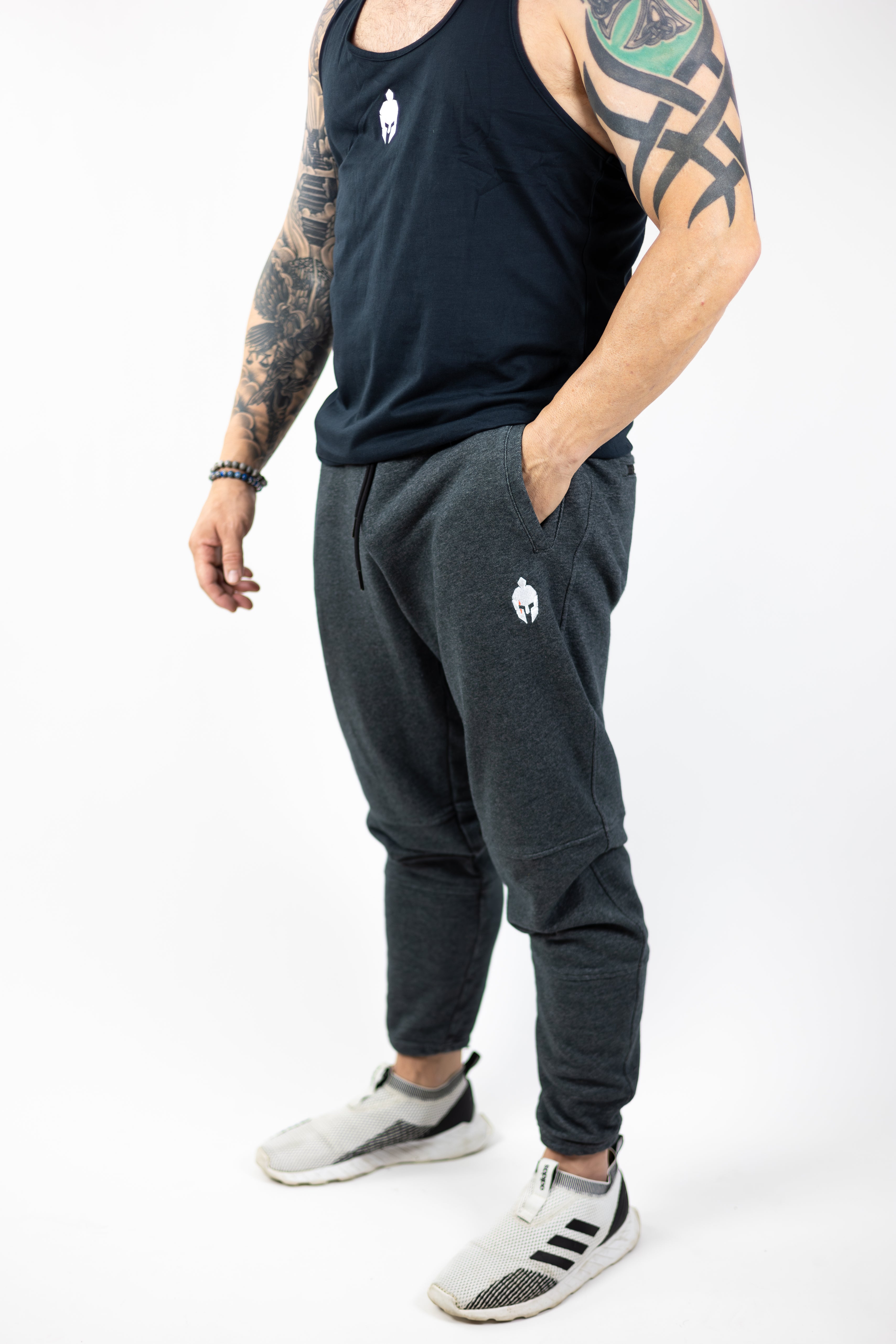 man modeling Strength of One gray sweatpants with embroidered helmet logo at top right hip and Strength of One logo vertical down left lower leg