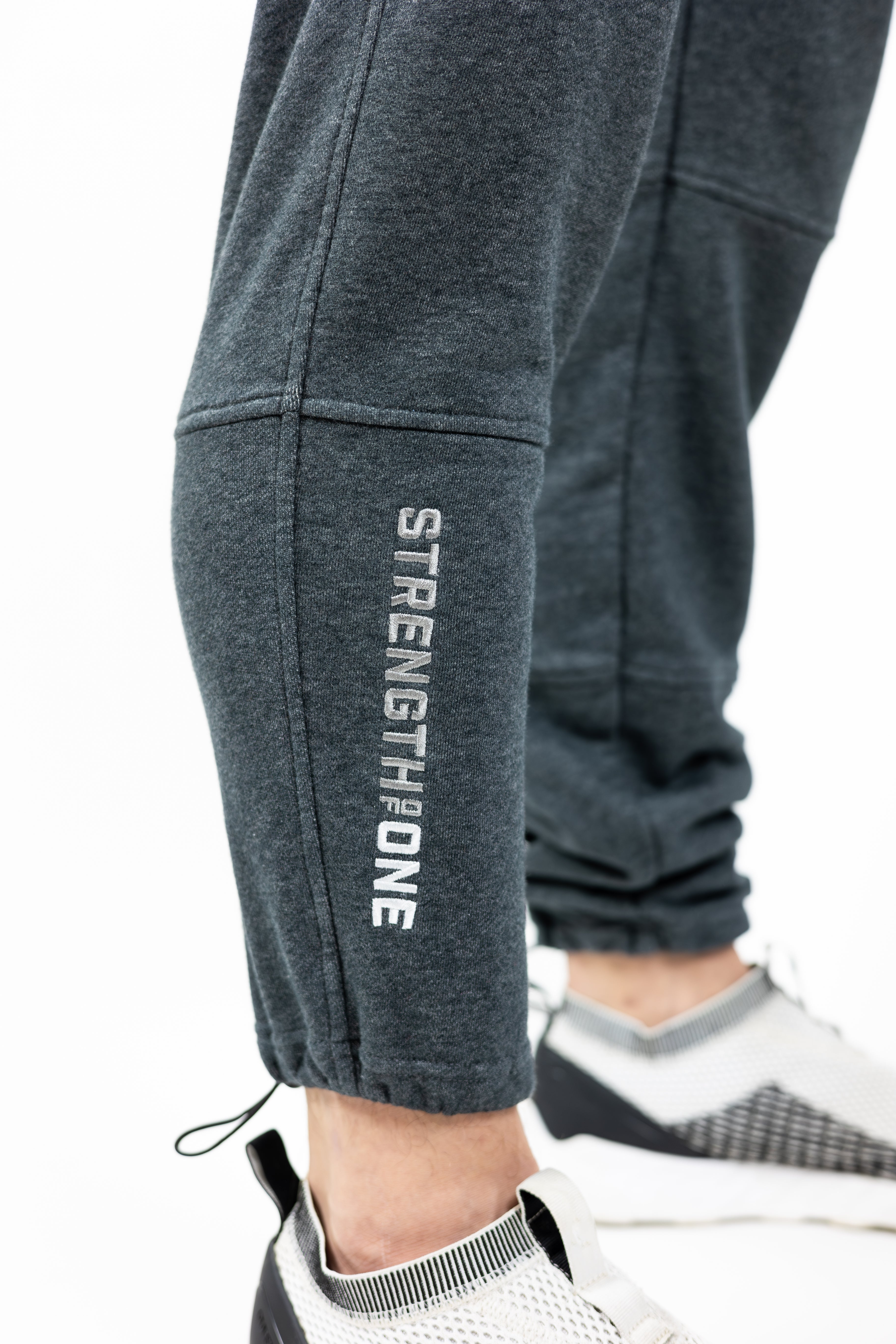 man modeling gray sweatpants with embroidered Strength of One logo vertical down left lower leg