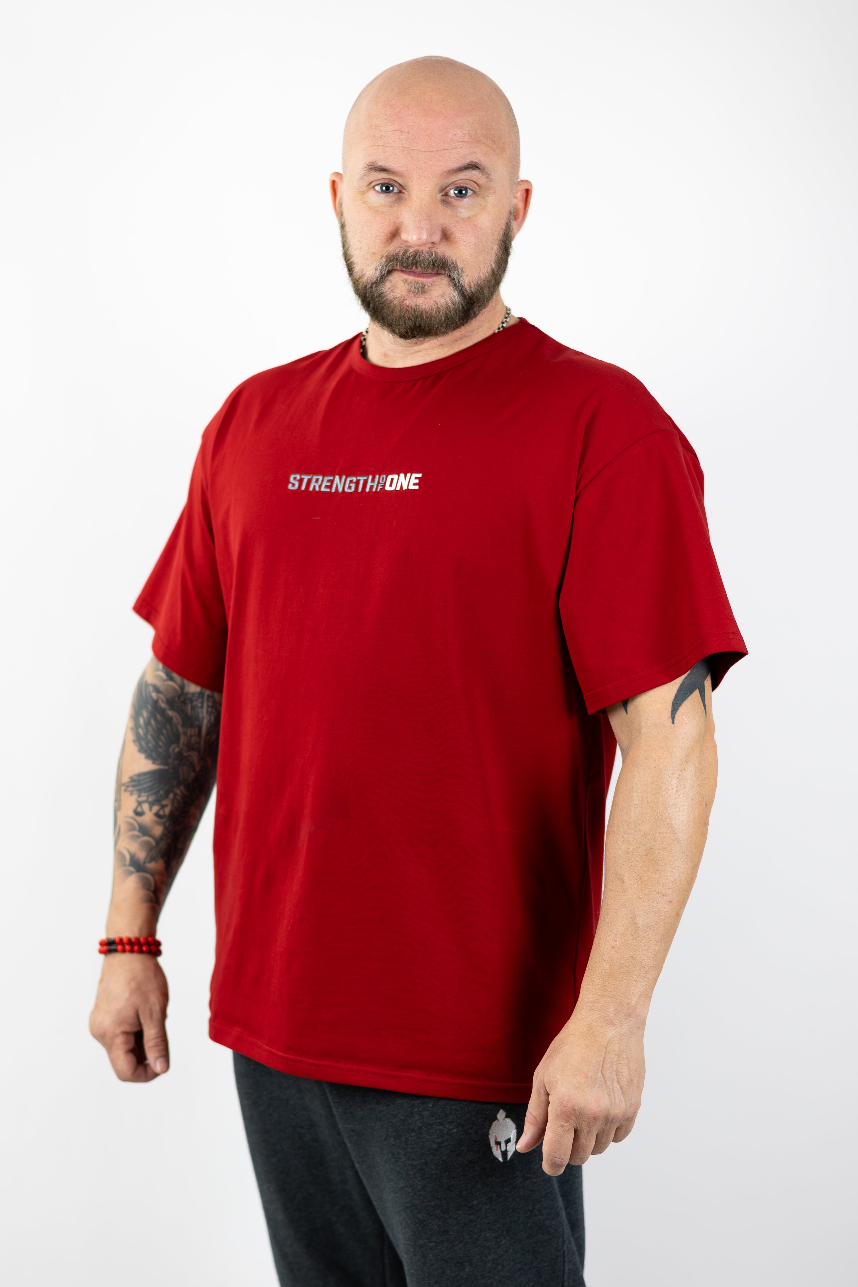 man modeling red workout shirt with an embroidered logo reading Strength of One