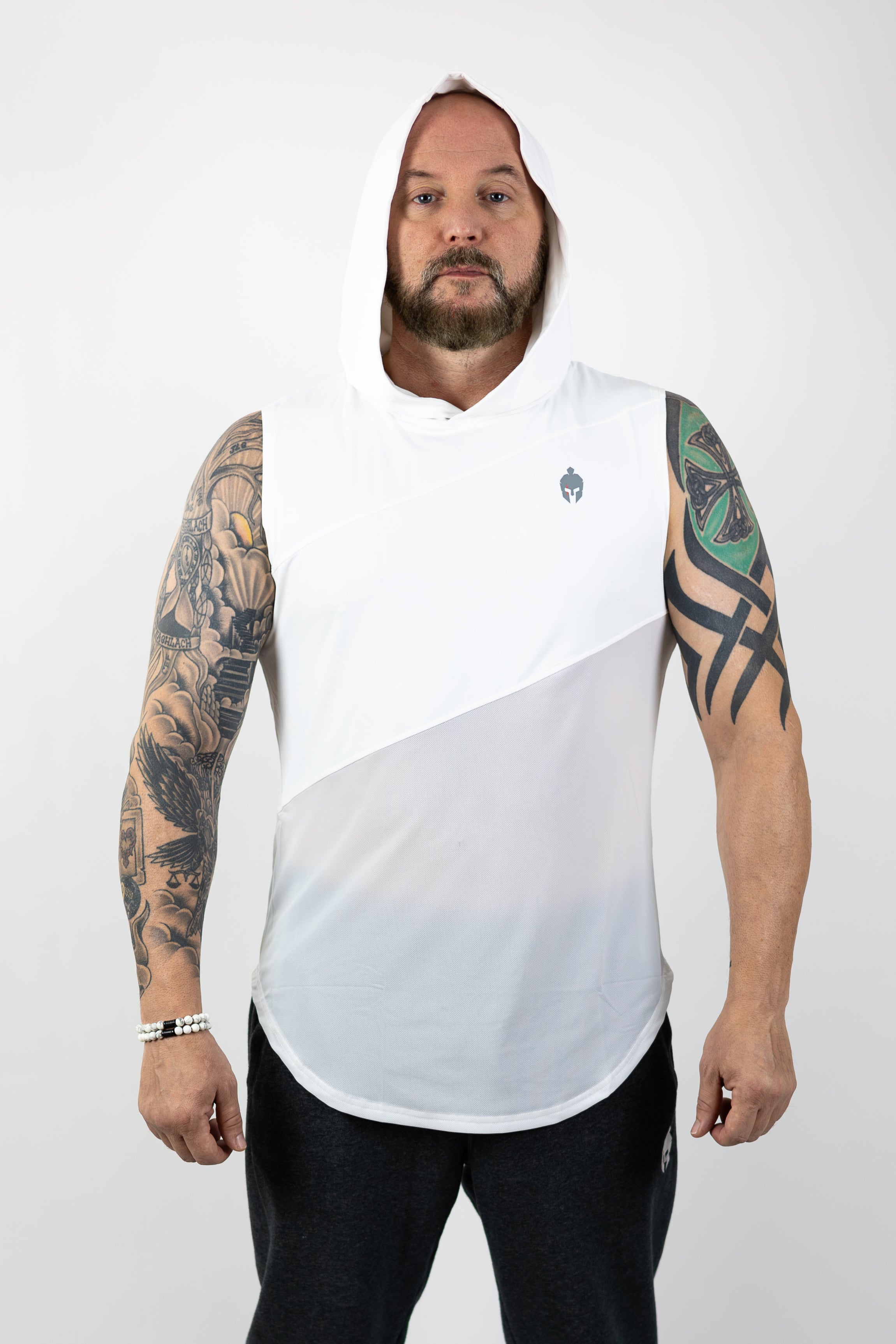 A man with tattoos on his arms stands confidently in a white Strength of One shirt with hood over head and gray sweatpants