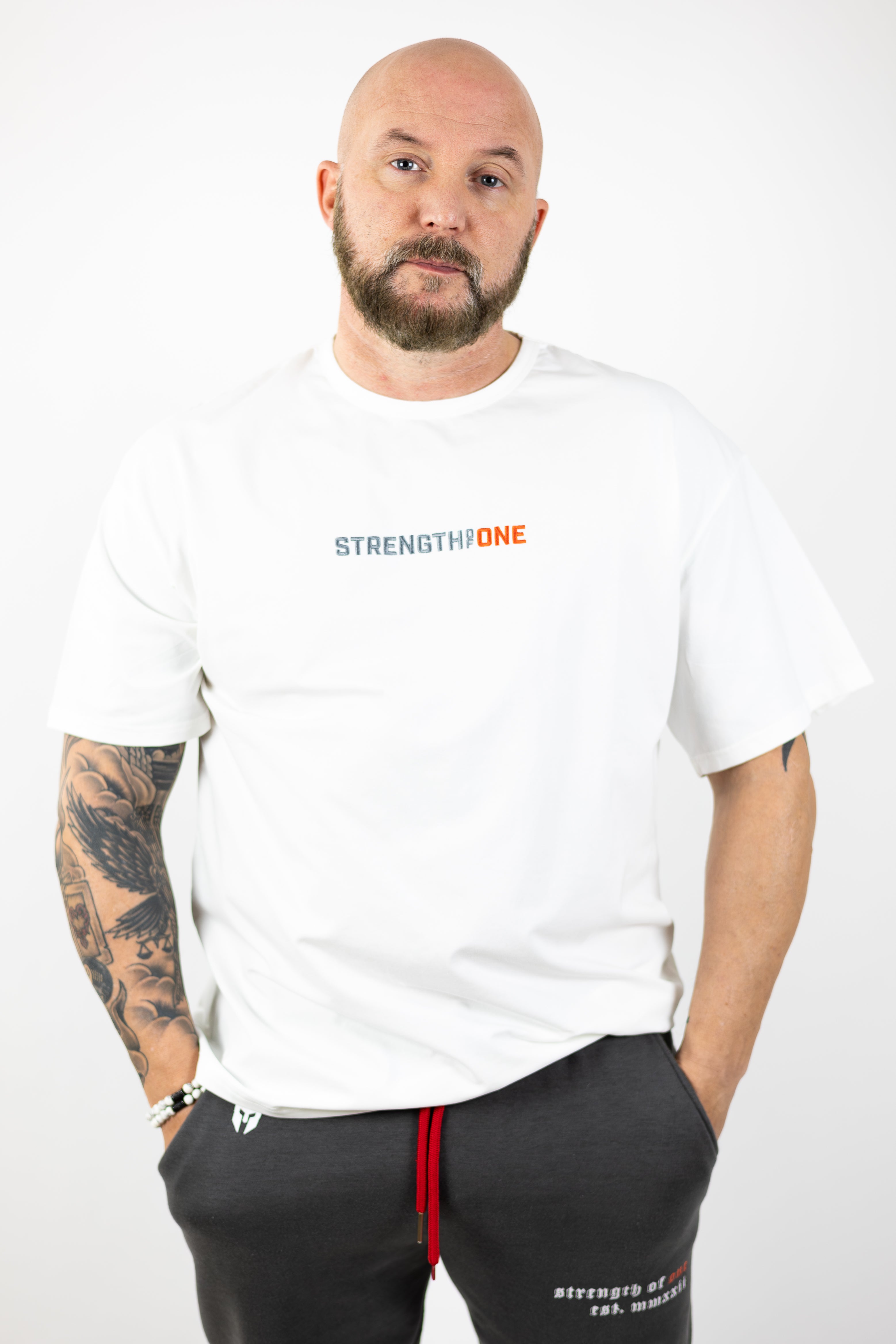 man modeling white Strength of One workout shirt with an embroidered logo reading Strength of One and gray sweatpants