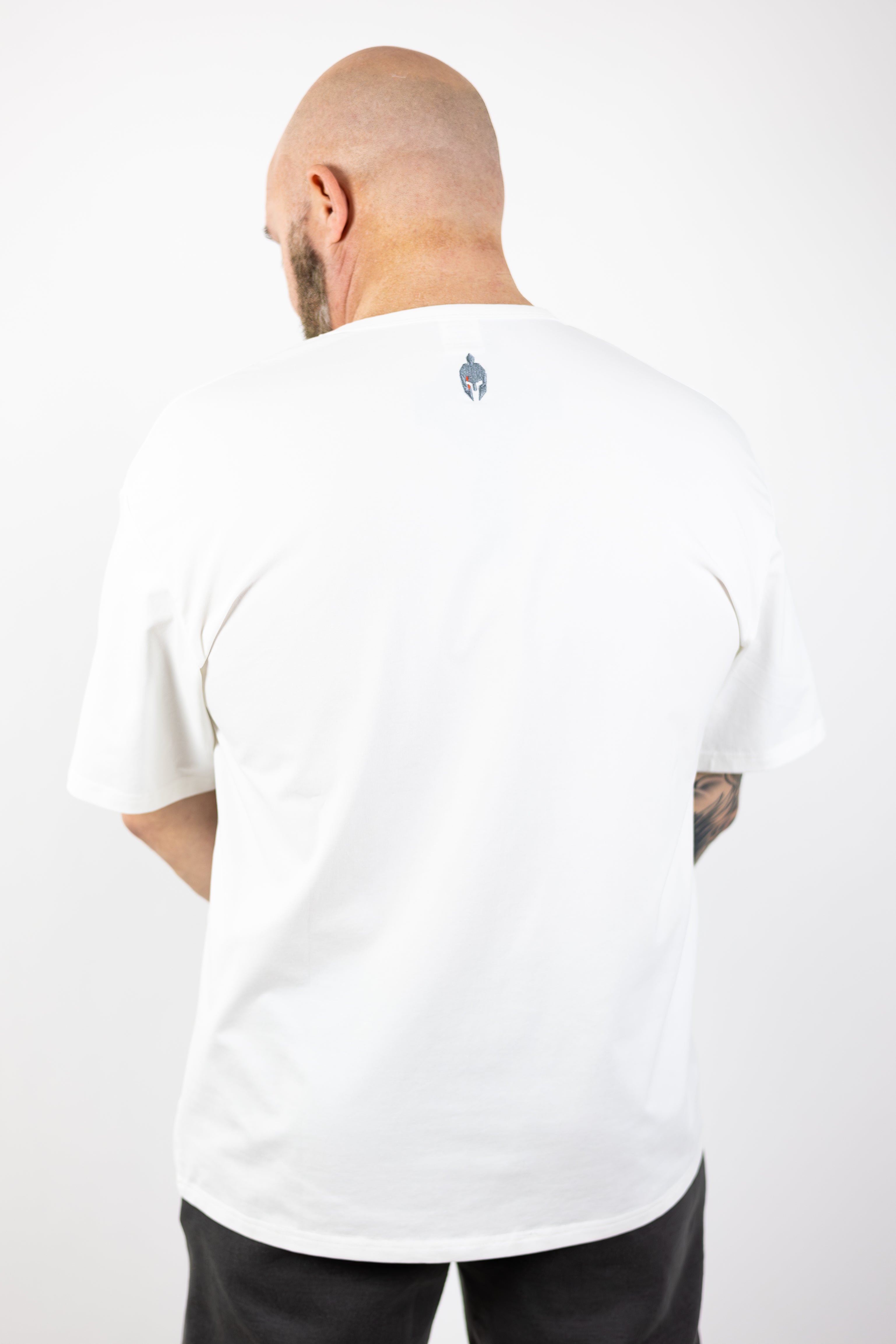 man turned around modeling Strength of One white workout shirt with helmet logo embroidered on top back neck