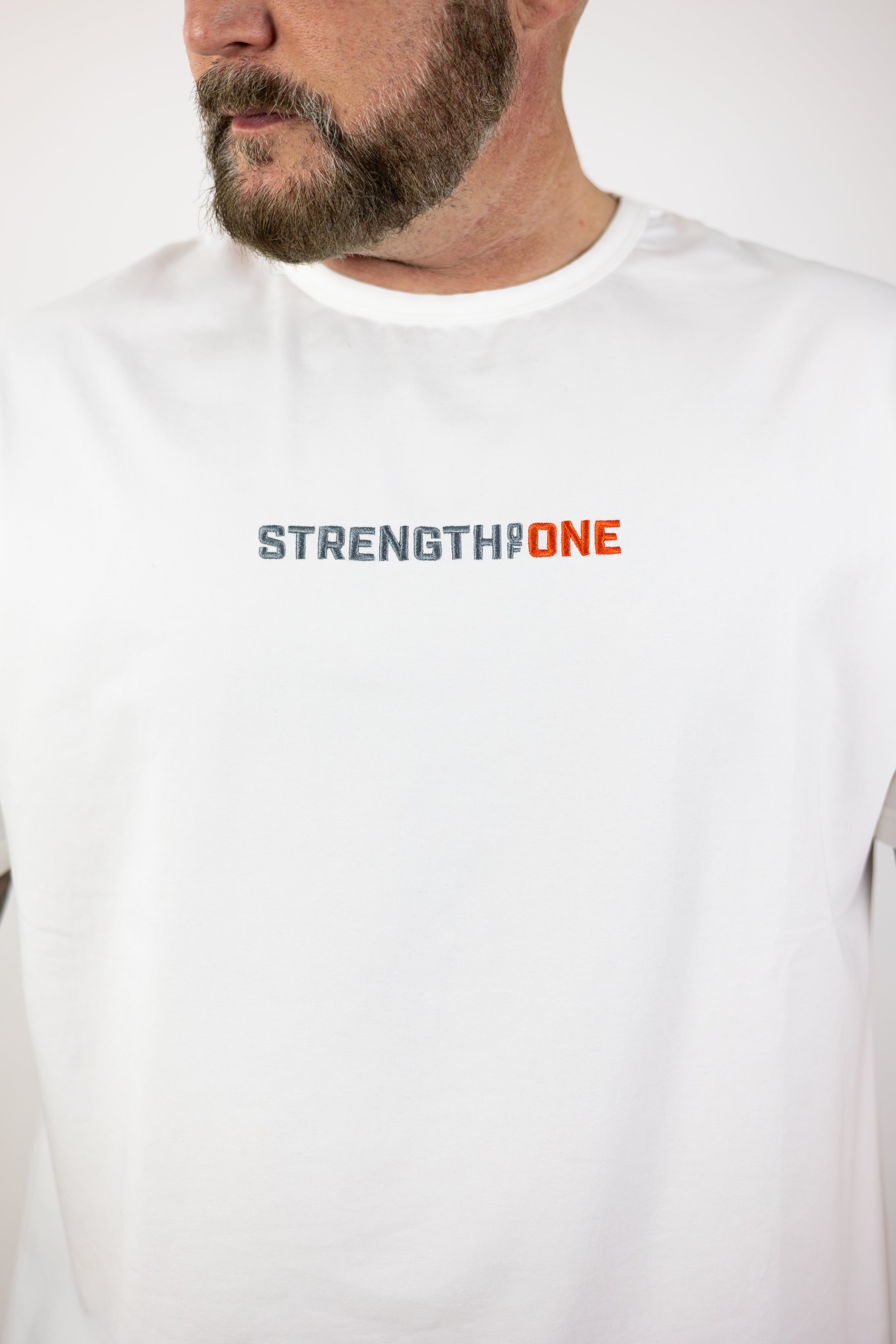 man modeling Strength of One white workout shirt with an embroidered logo reading Strength of One