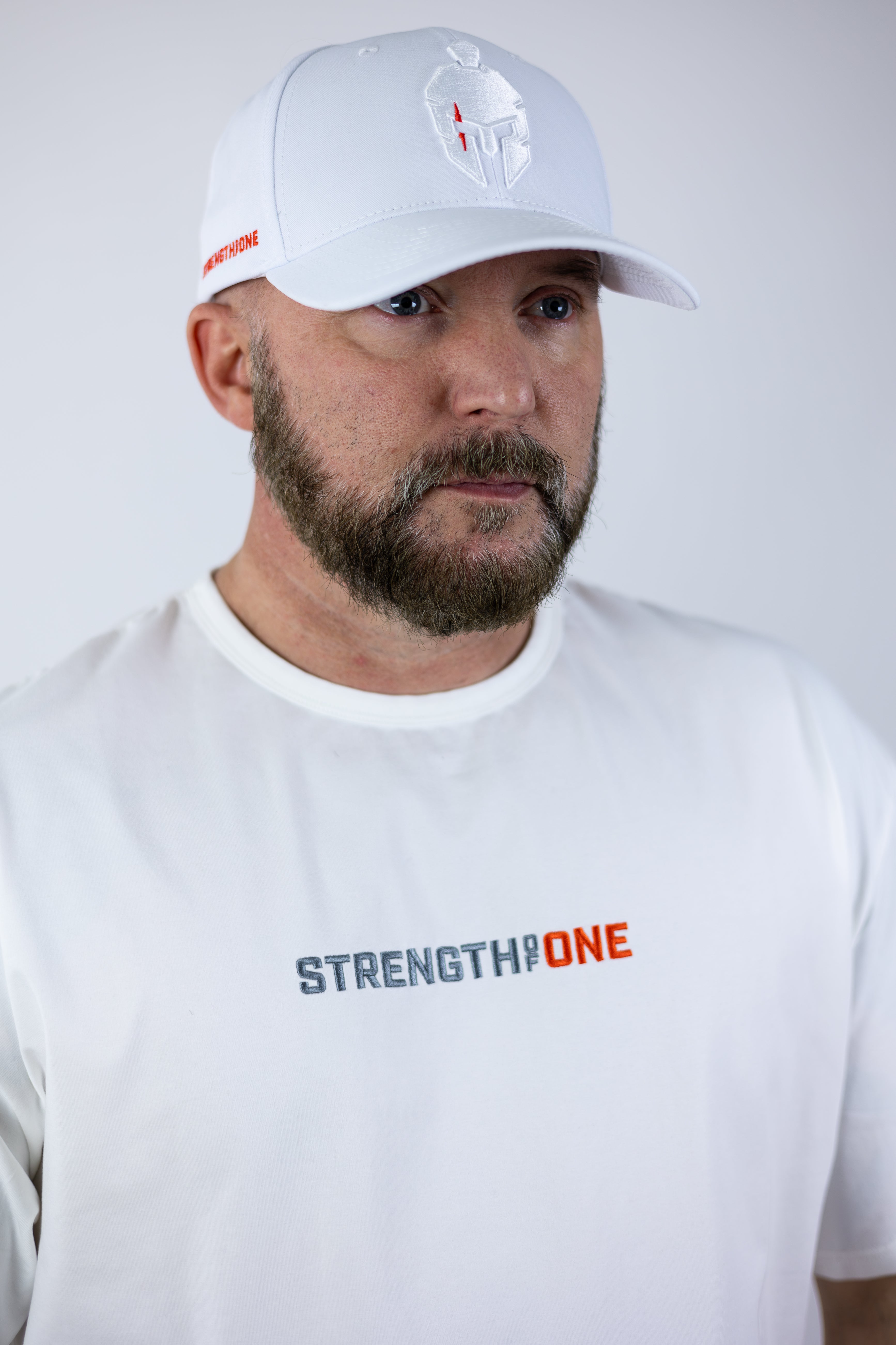 man wearing white Strength of One gym shirt and white baseball hat with warrior helmet logo on front