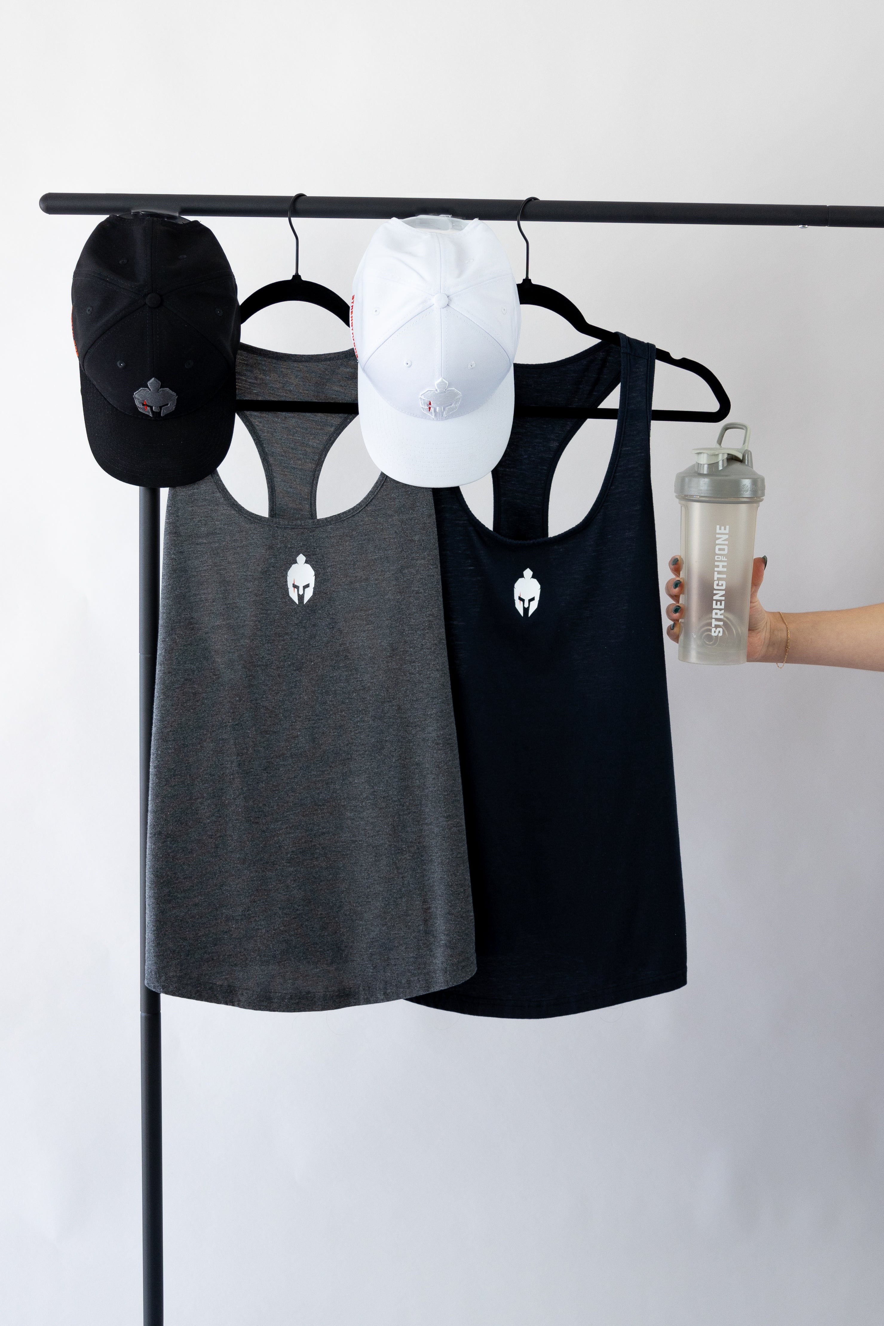 Two Strength of One workout stringers, two Strength of One hats, and Strength of One Blender Bottle hanging on a clothing rack