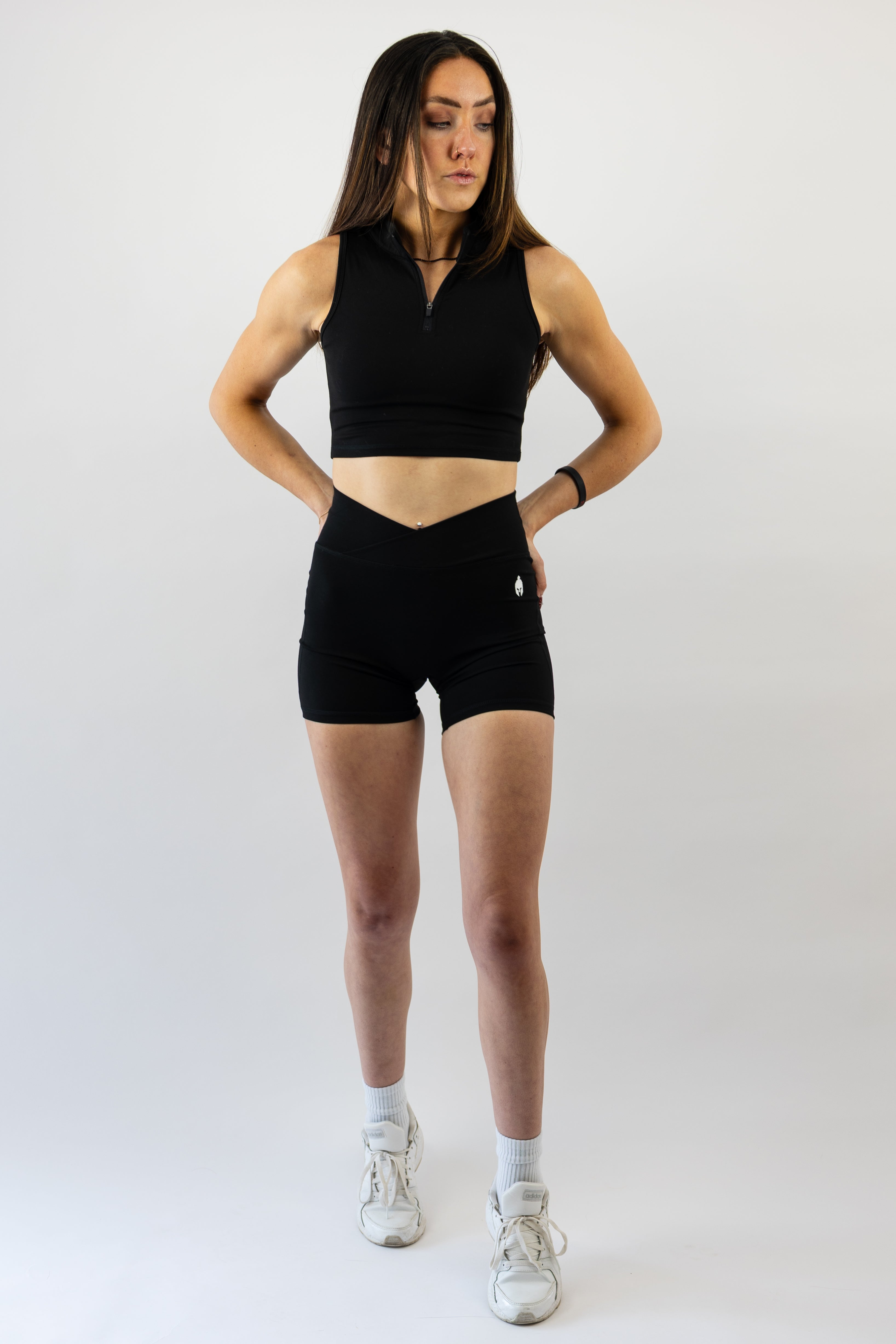 Woman wearing a black Strength of One workout outfit with white sneakers on a plain background