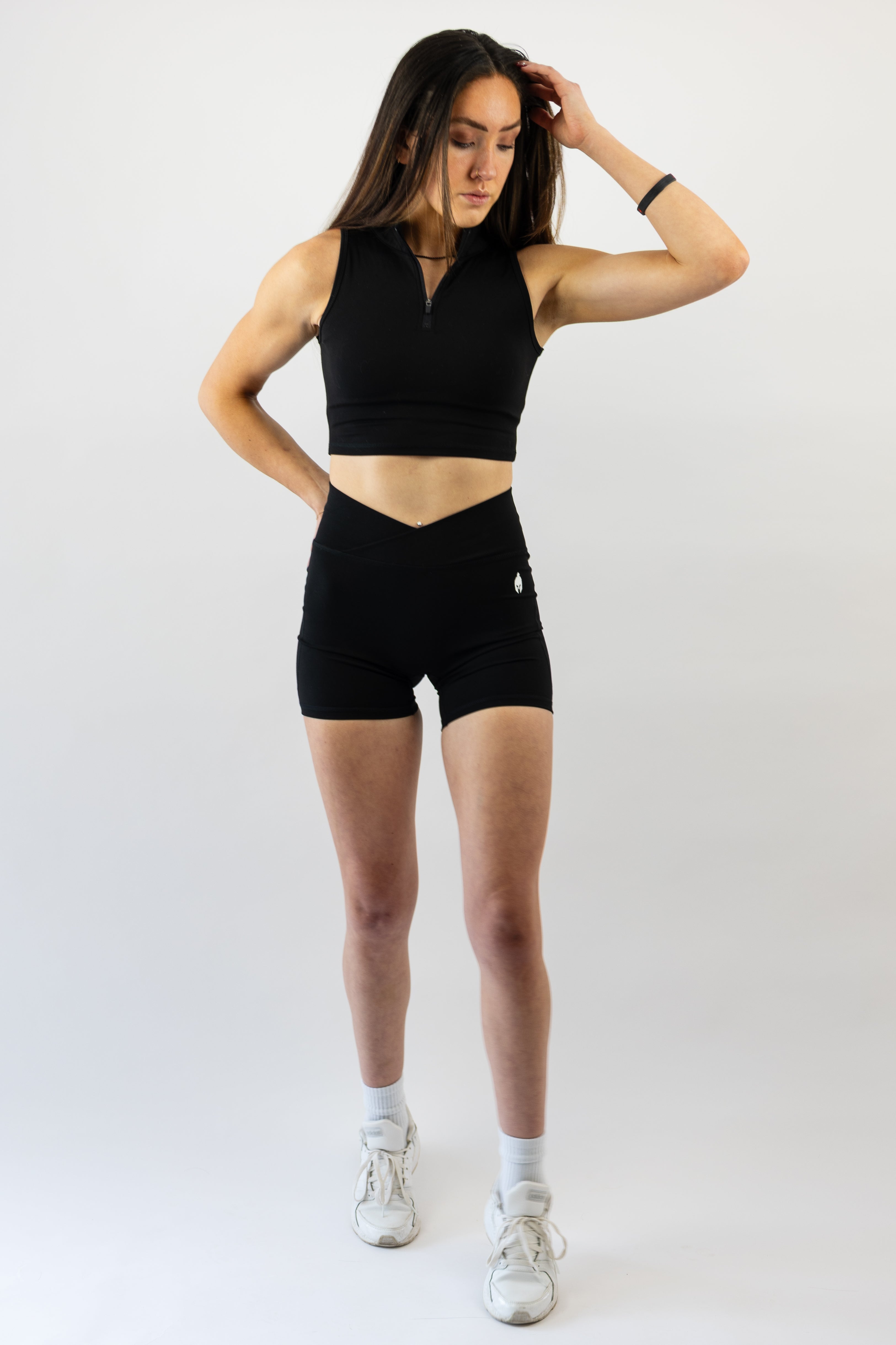 Woman wearing a black Strength of One workout outfit with white sneakers on a plain background