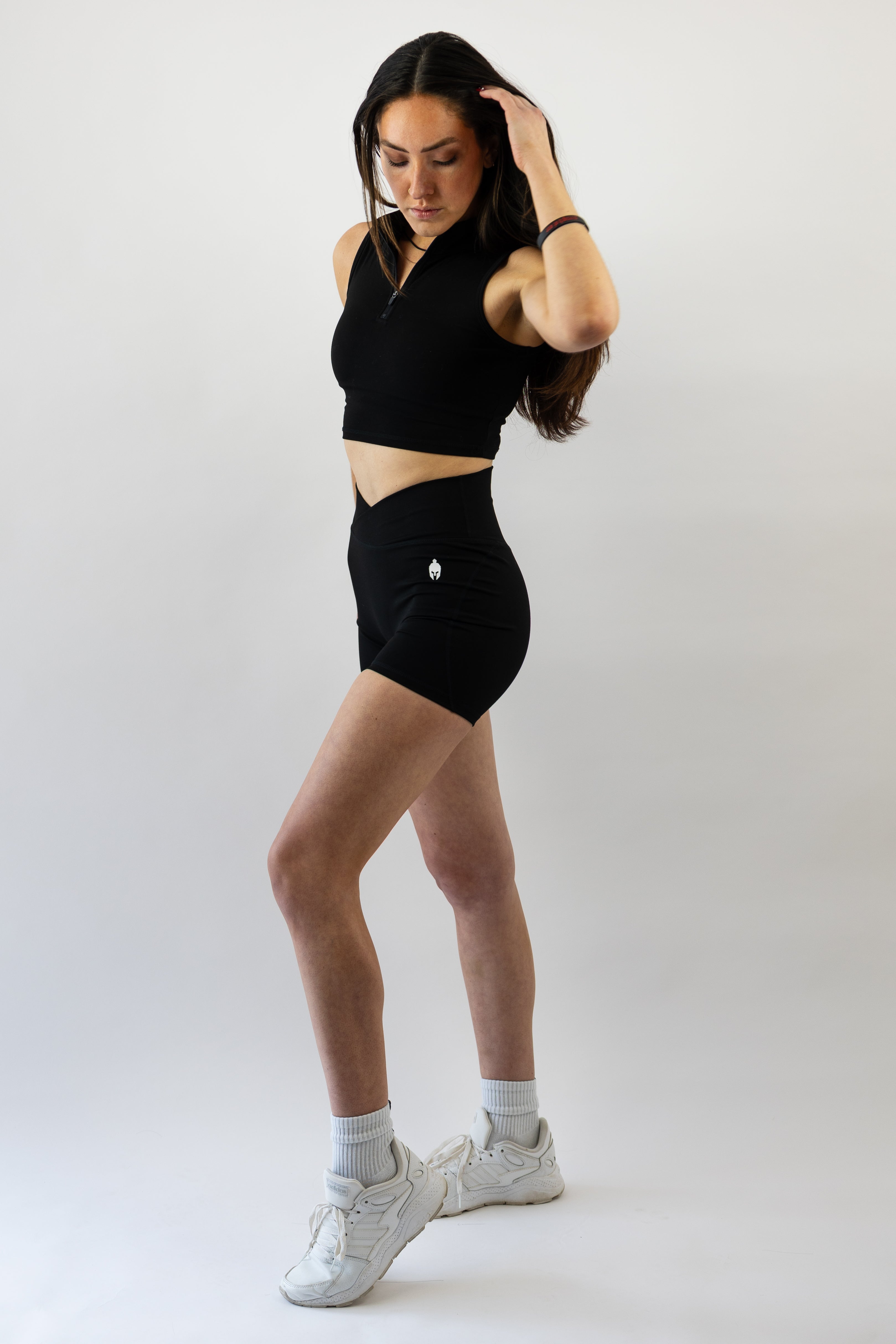 Woman wearing a black Strength of One workout outfit with white sneakers on a plain background