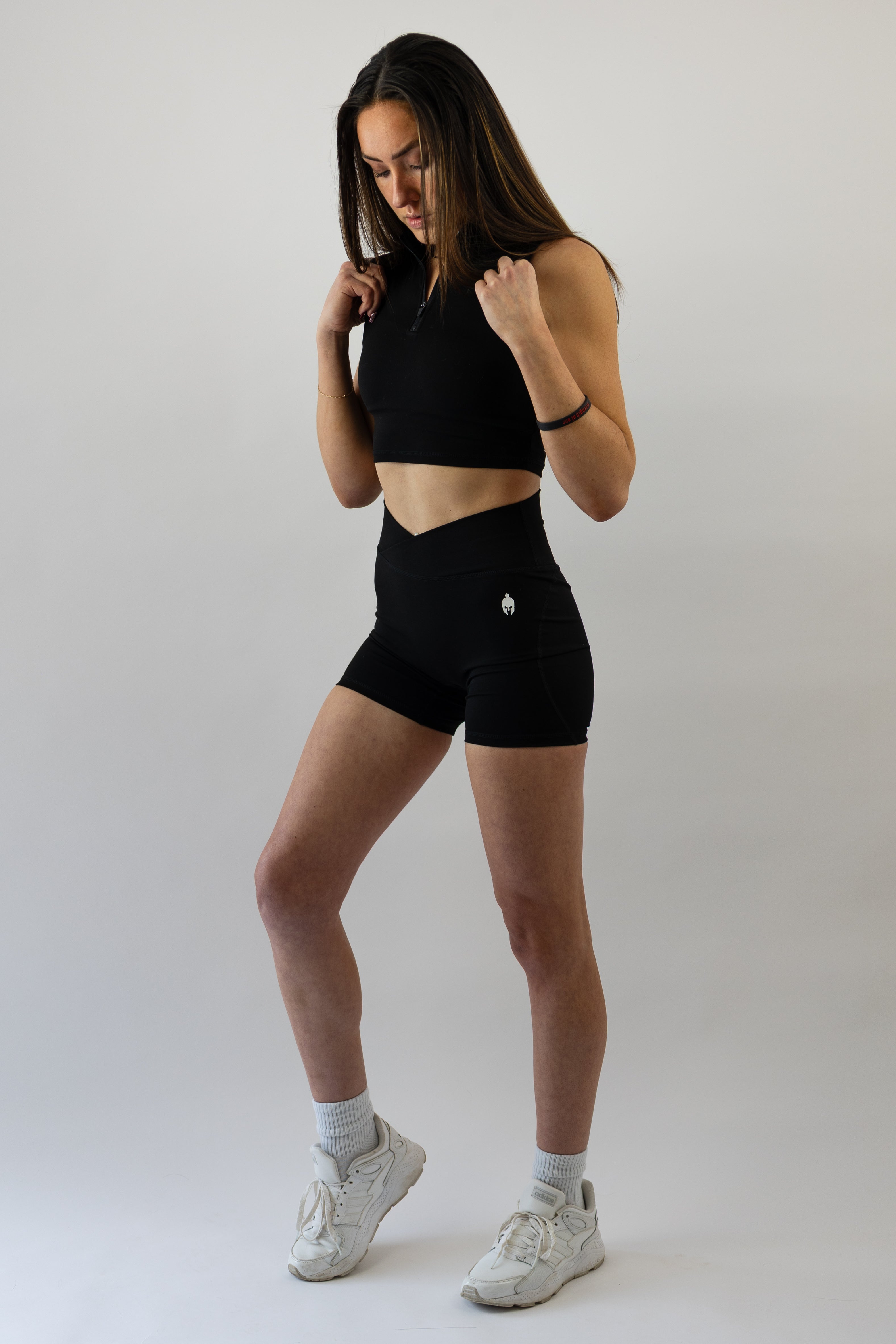 Woman wearing a black Strength of One workout outfit with white sneakers on a plain background