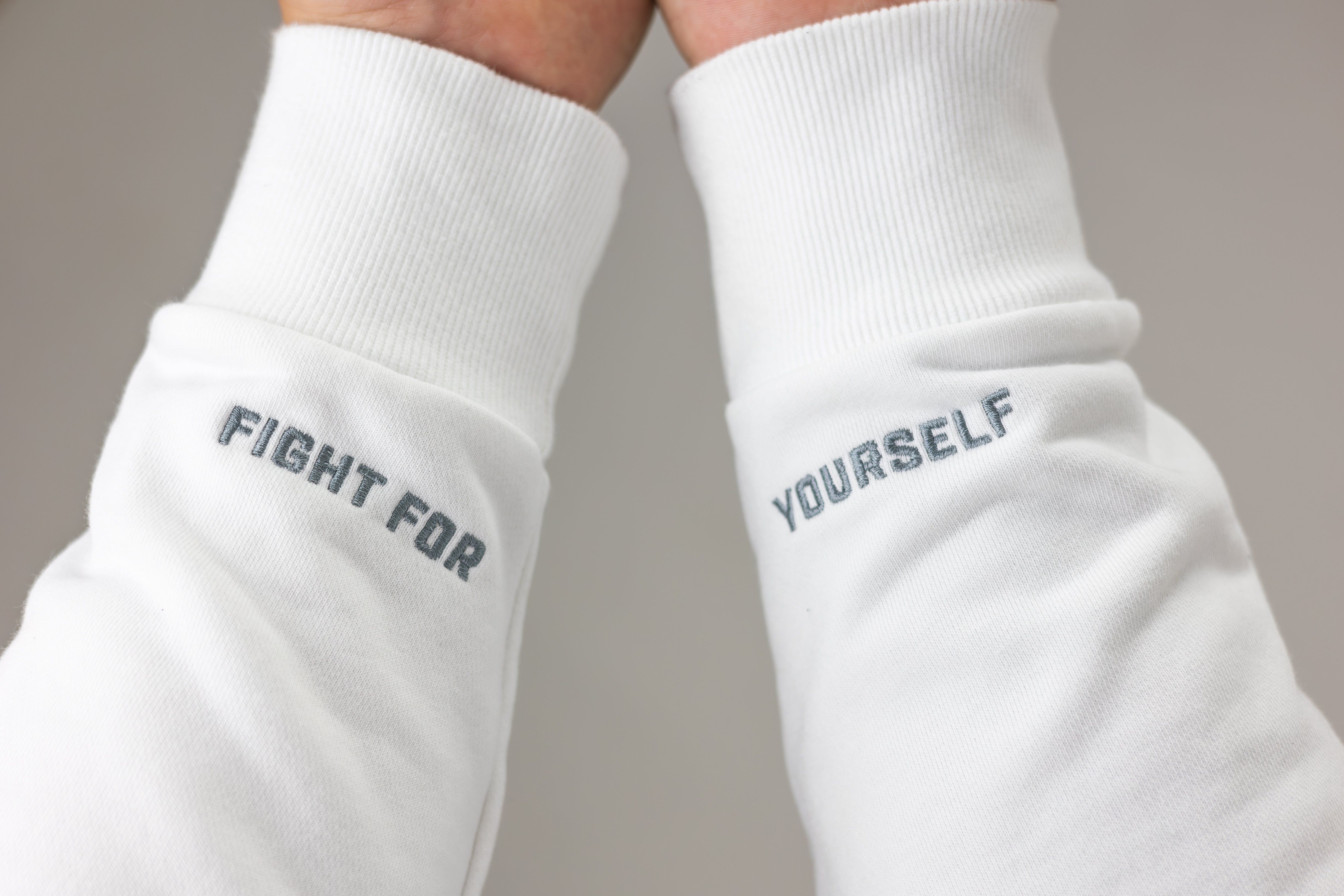 Detail photo of sleeves of white Mantra Hoodie that has "Fight For" embroidered on the left wrist and "Yourself" embroidered on the right wrist